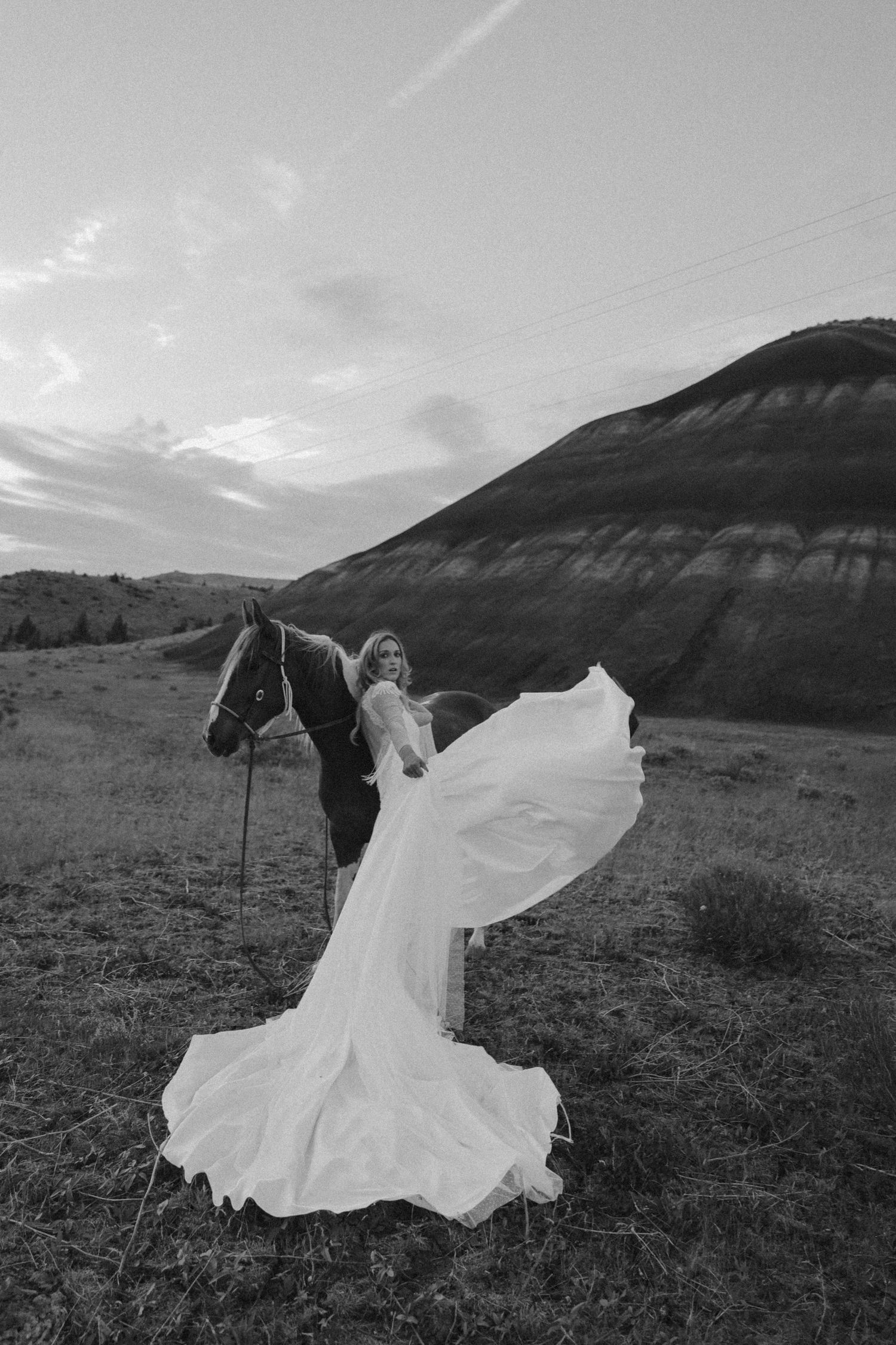 A dramatic black and white wedding photo with flowing dress against mountain landscape.