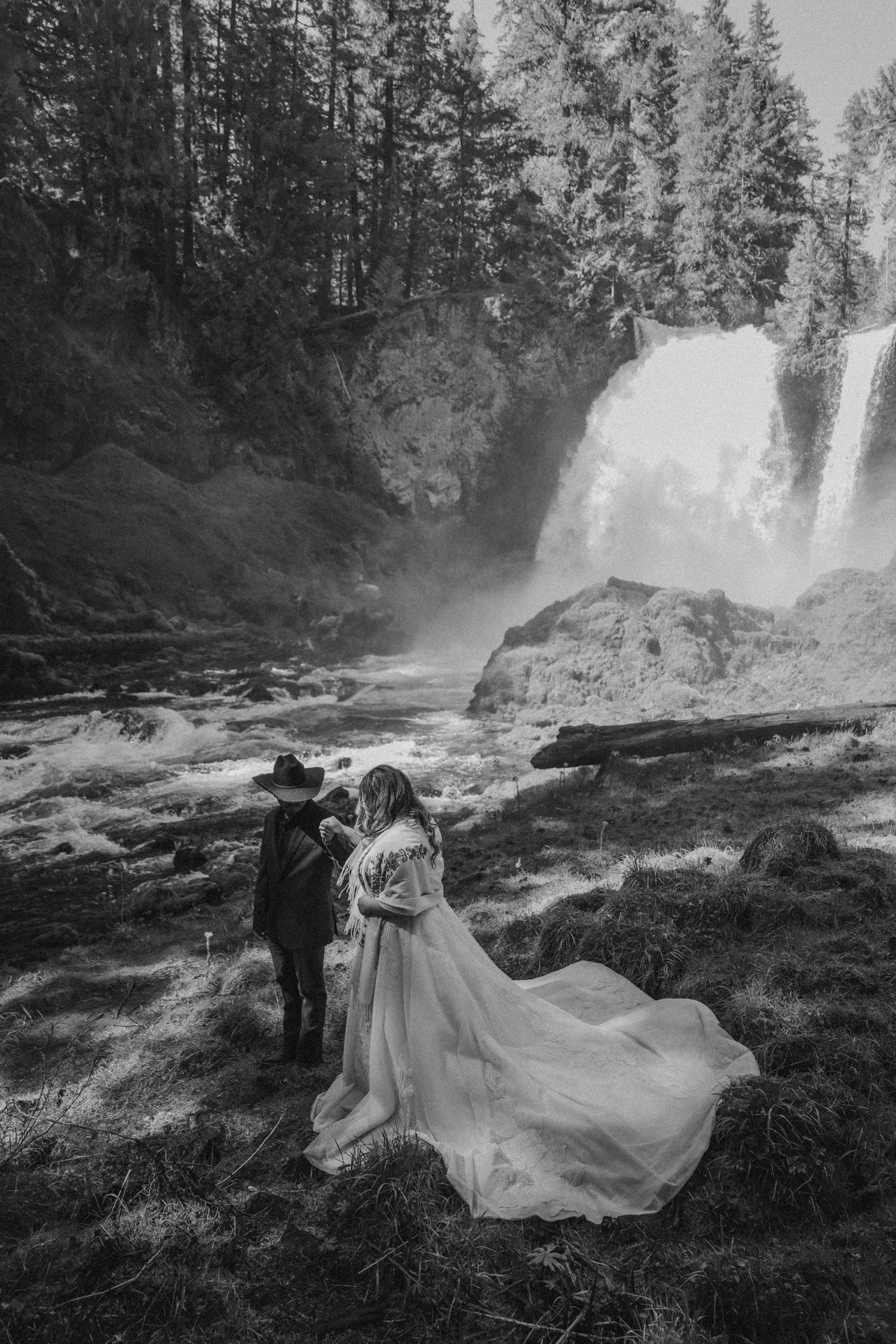 Black and white wedding photography series near a dramatic waterfall with flowing dress movements.