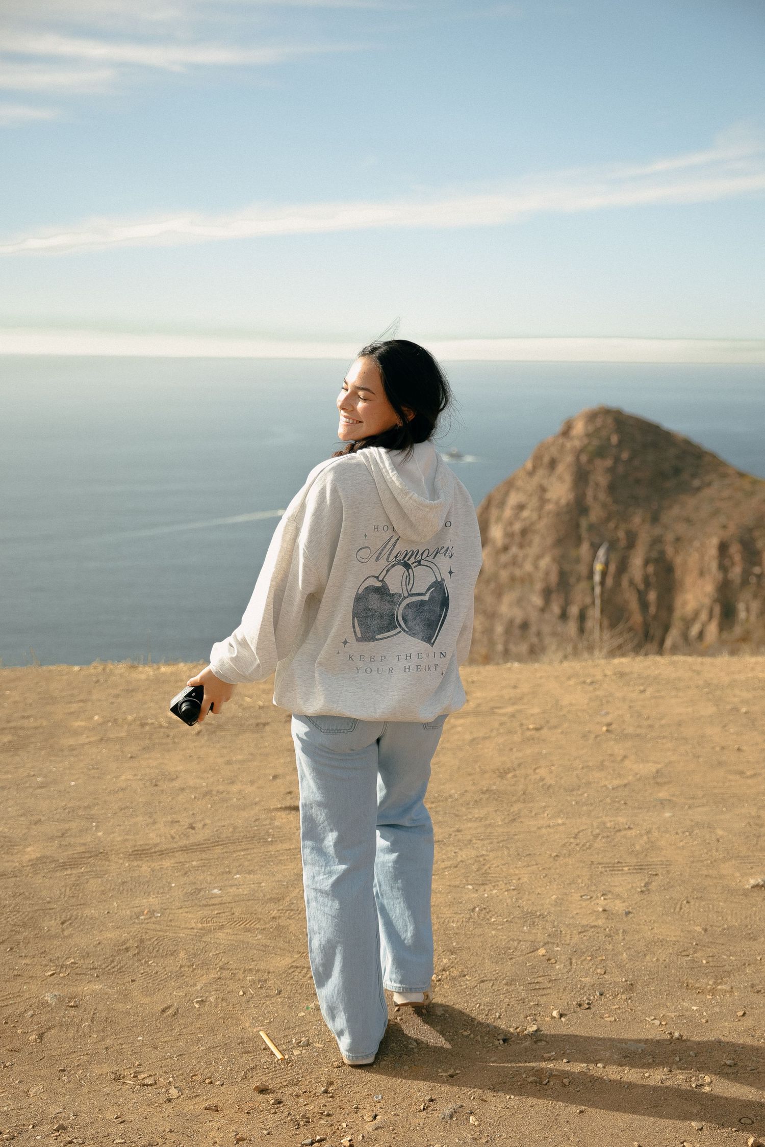 Person wearing white sweater stands against coastal cliff backdrop.
