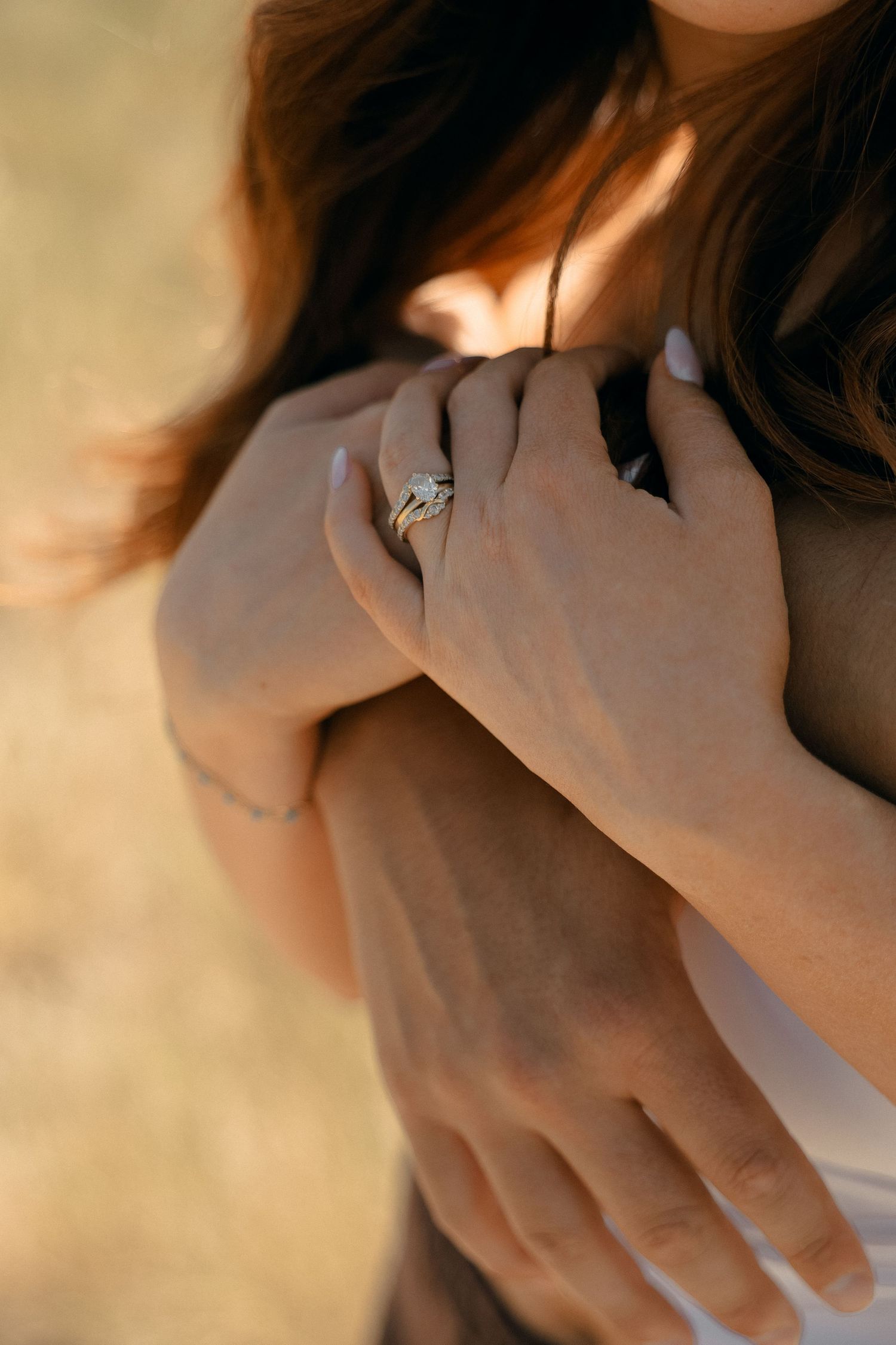 A close-up shot of hands wearing a diamond engagement ring in warm sunlight.