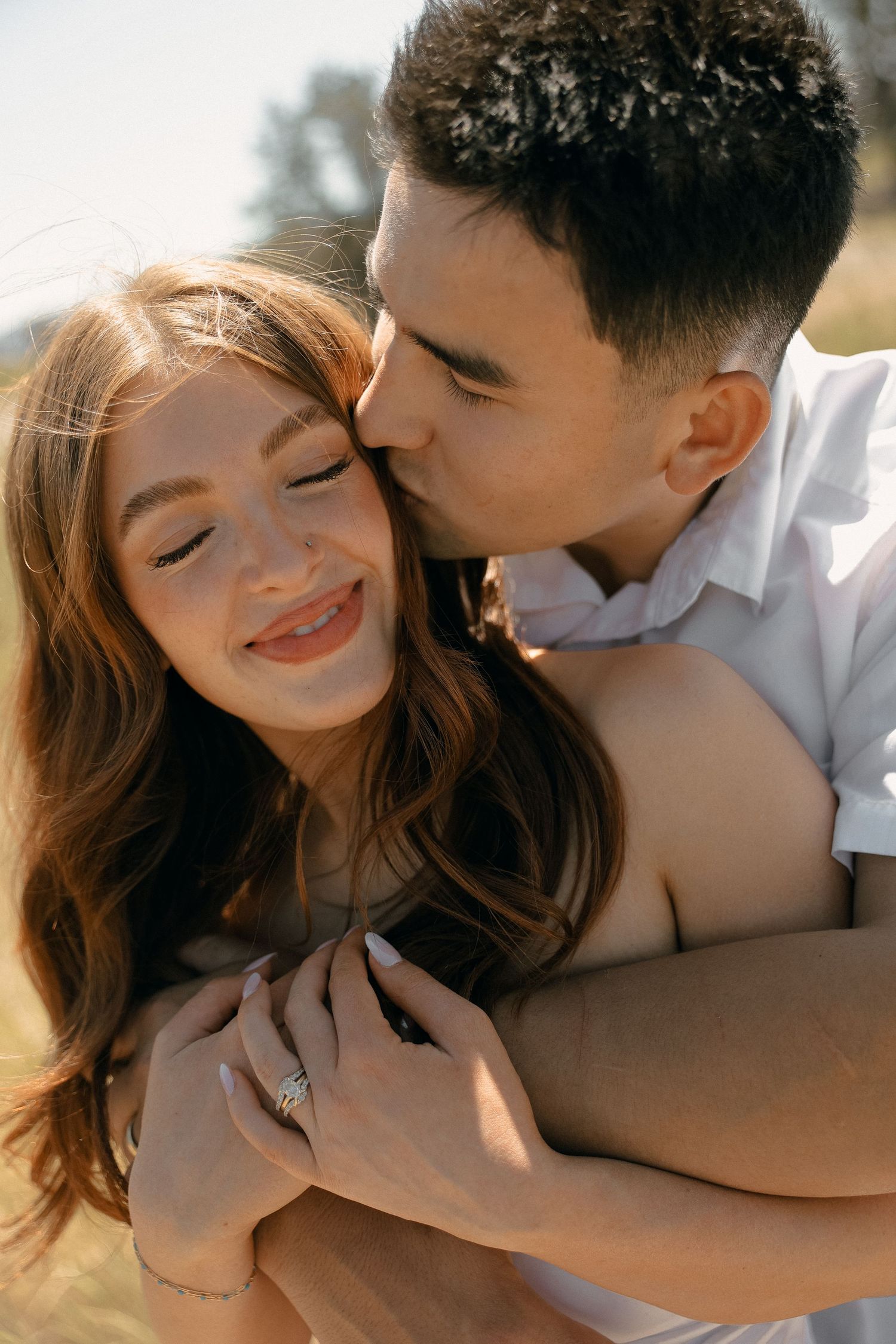 Intimate sunlit couple embraces outdoors, showing affection with a kiss while sharing a romantic moment together.