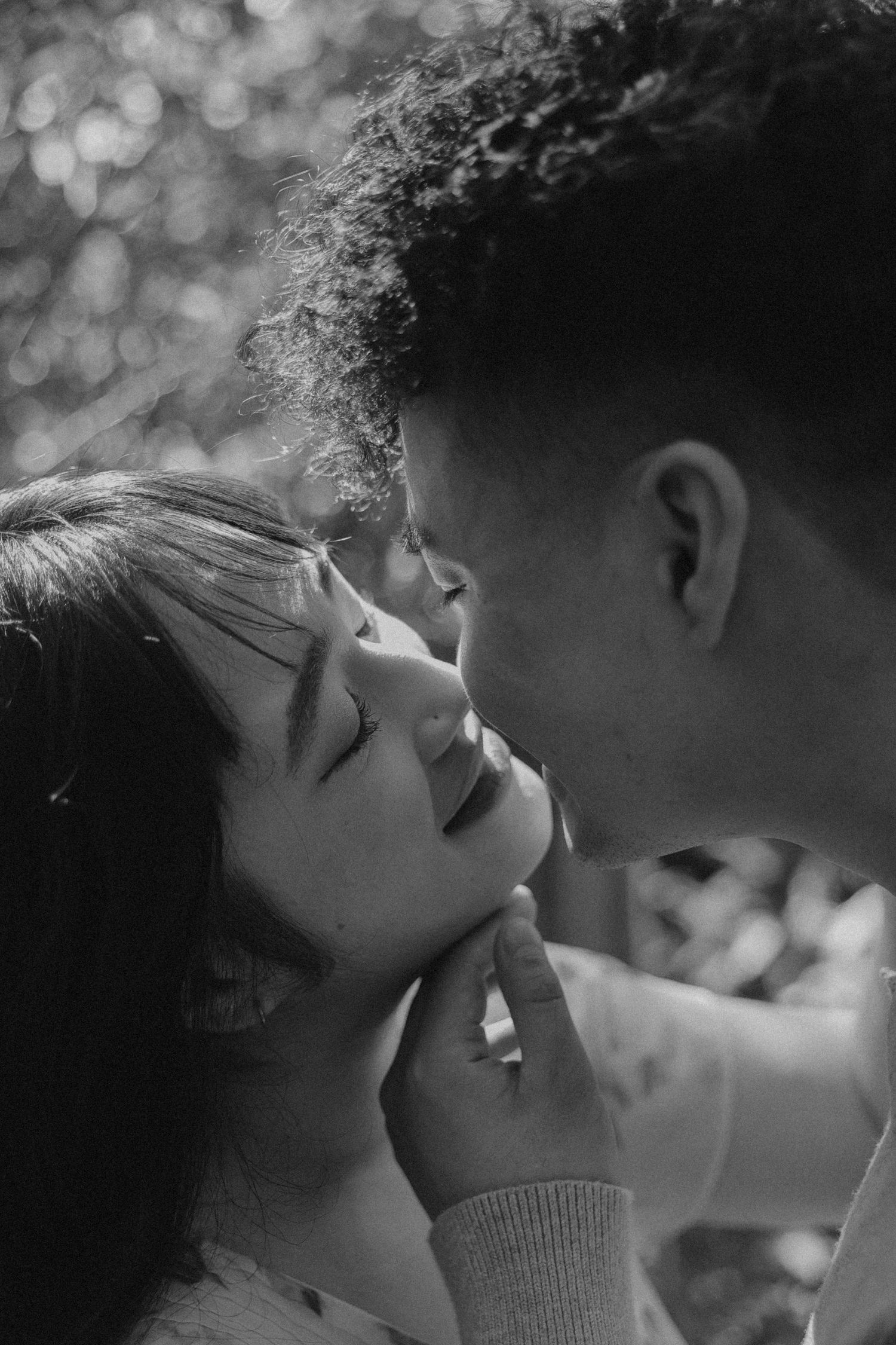Black and white intimate portrait of a romantic couple sharing a tender moment in soft bokeh lighting.