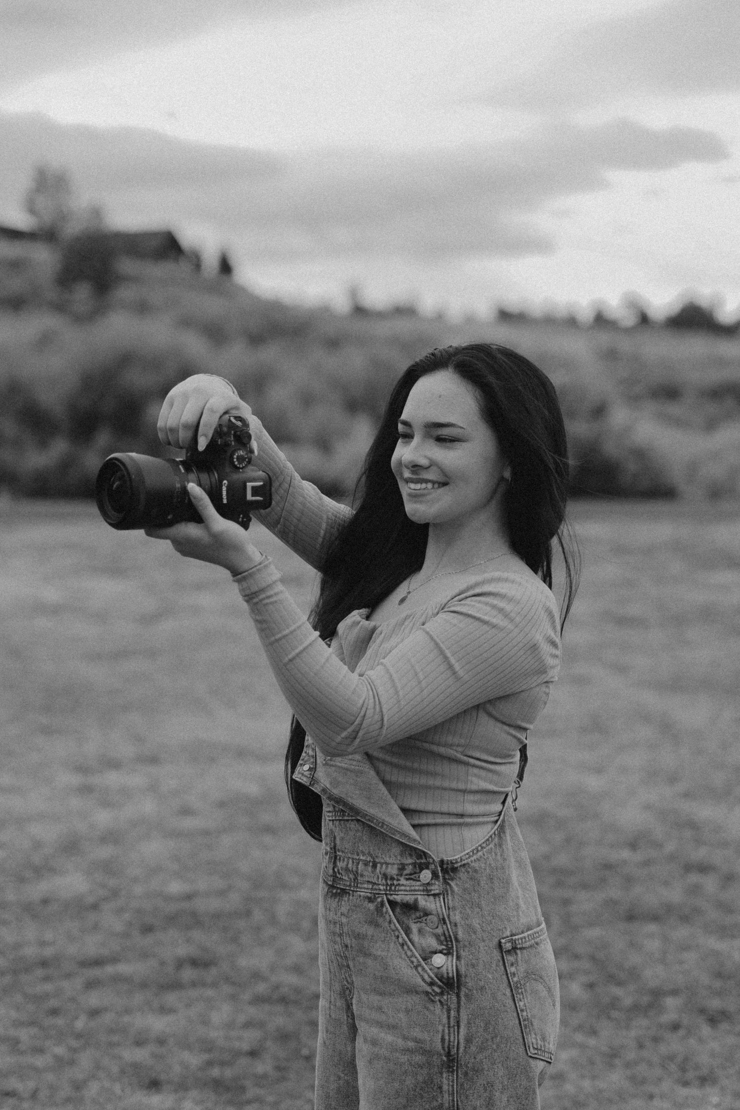 Photographer with long dark hair taking pictures with a professional camera in a field.