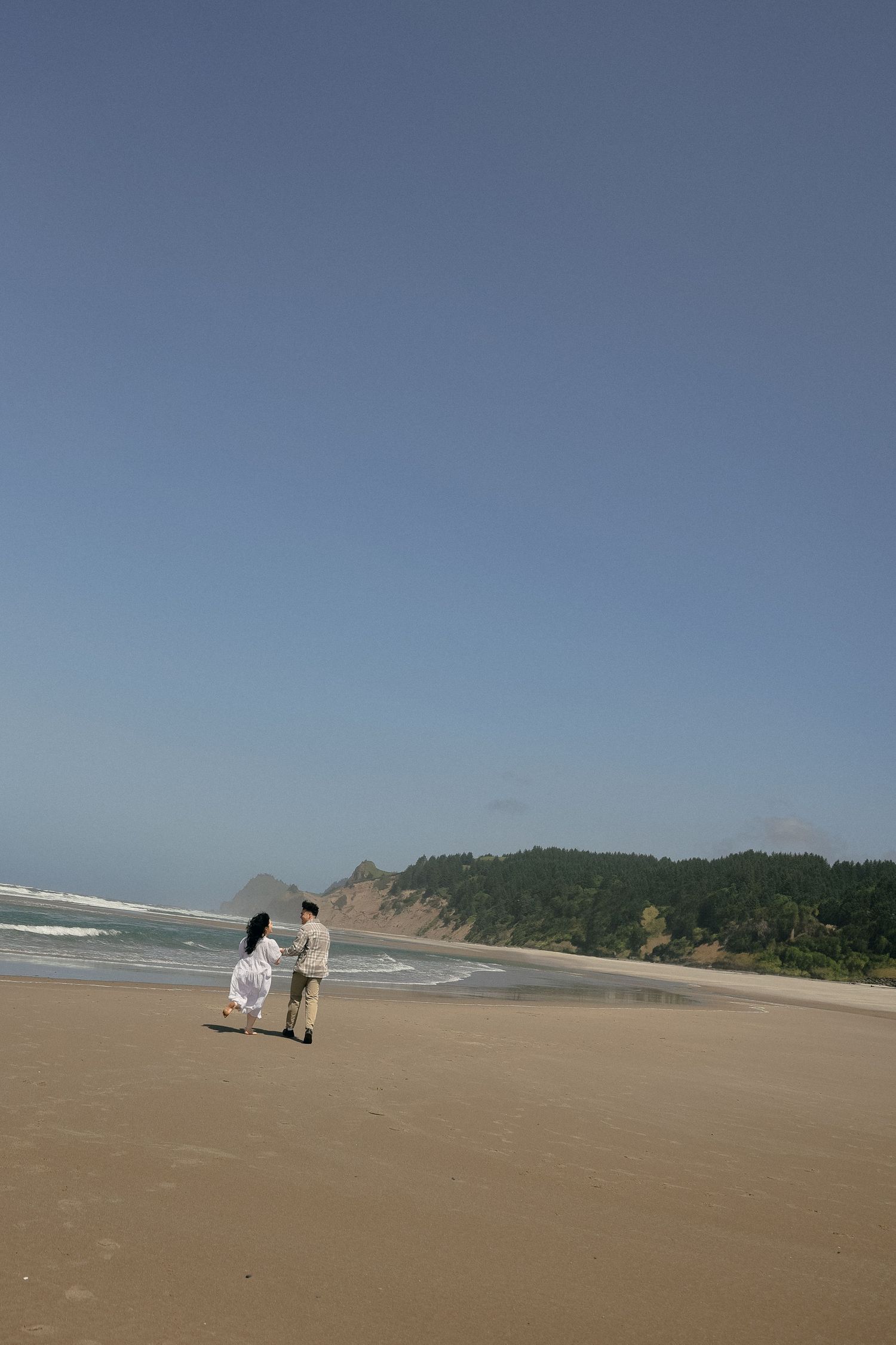 A wide shot of a serene beach landscape with distant figures walking along the shore.