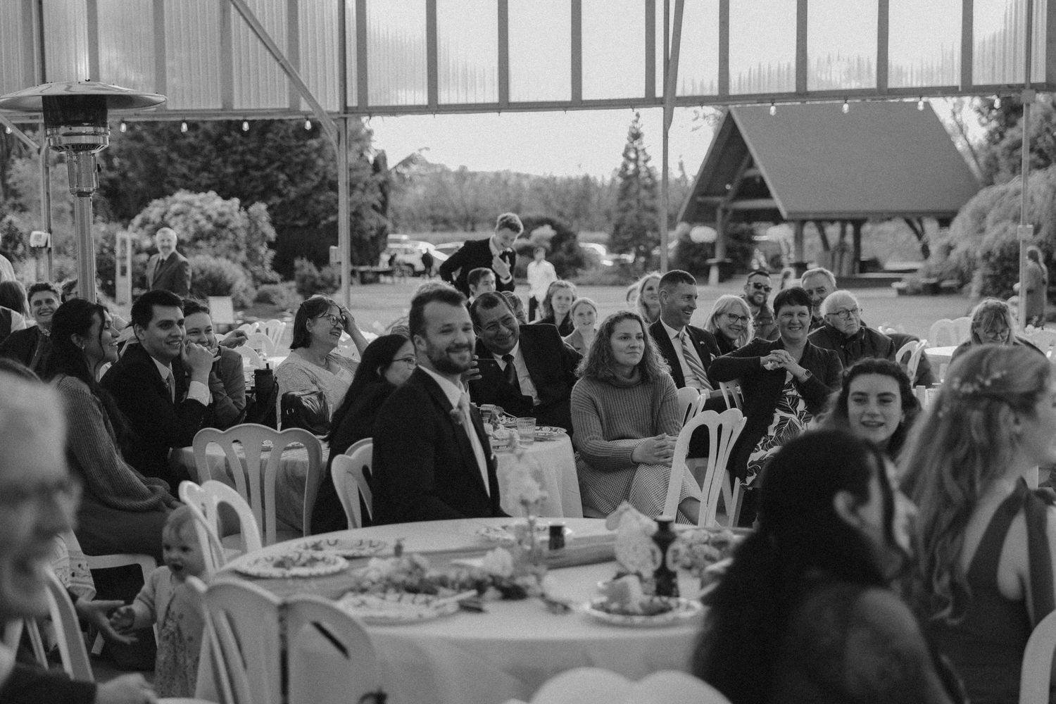 A black and white reception scene showing wedding guests gathered at dining tables.