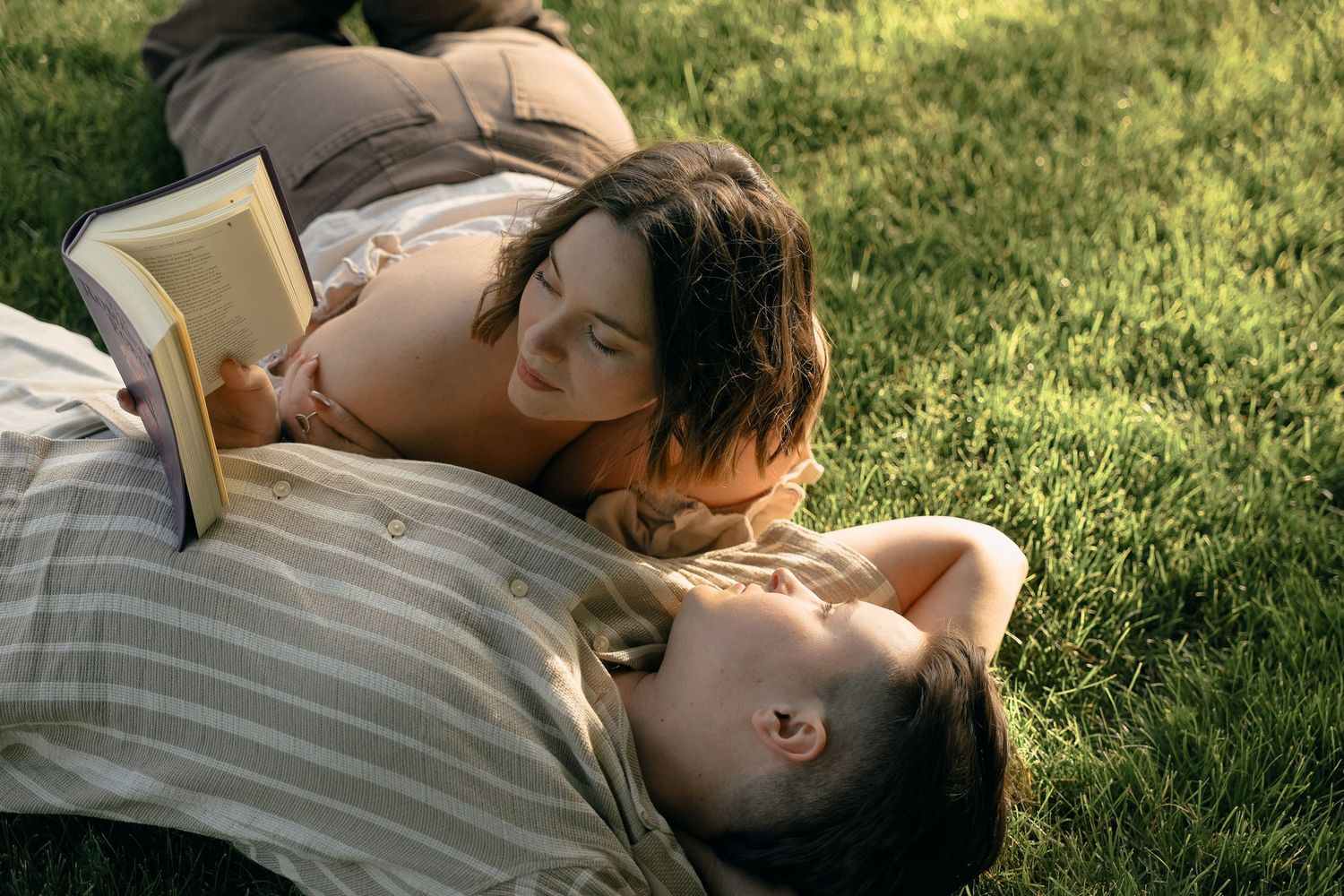 Romantic couple sharing an intimate moment while laying in green grass on a sunny day.