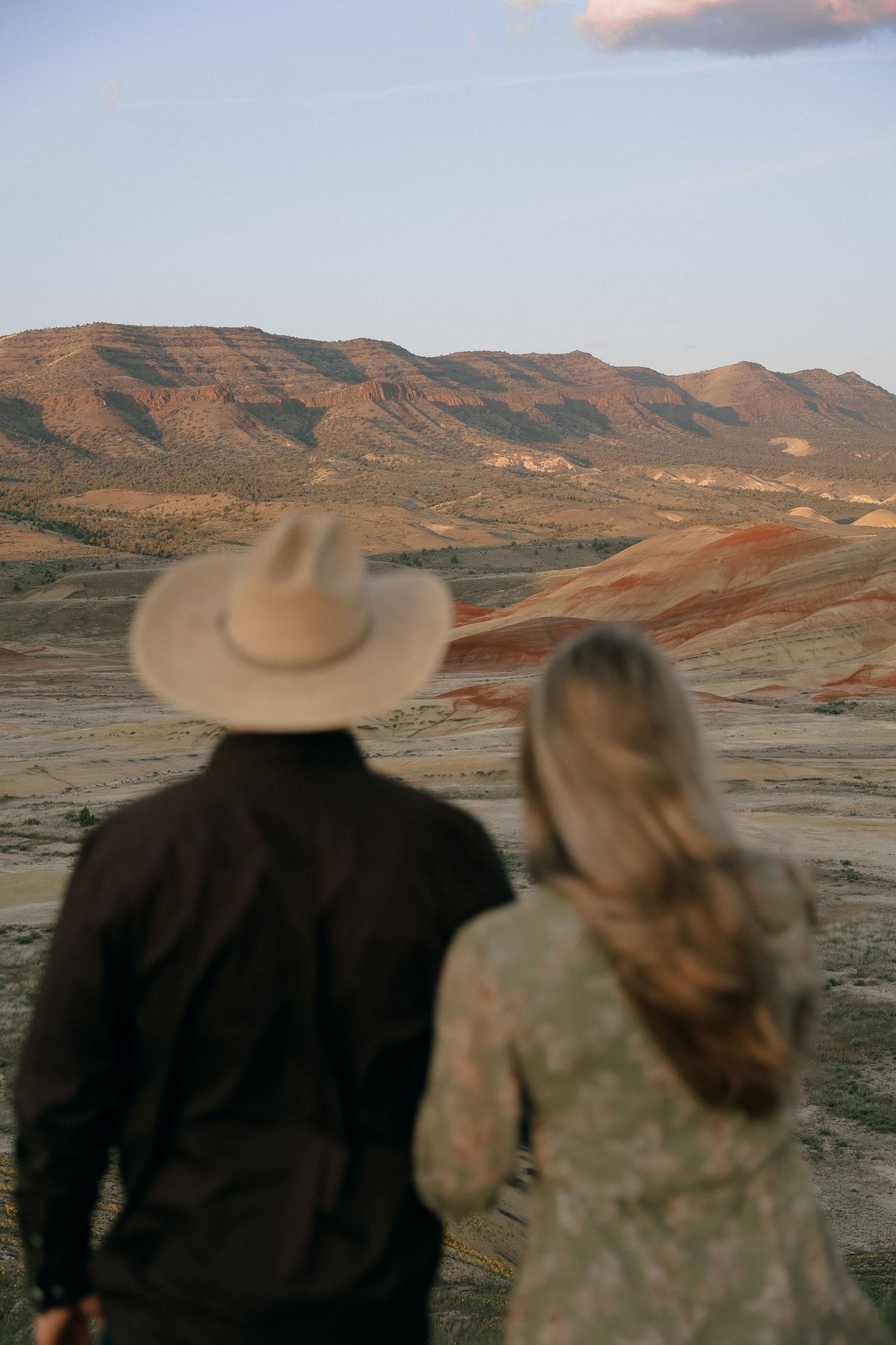 Couple viewing desert landscape while wearing western attire at sunset.