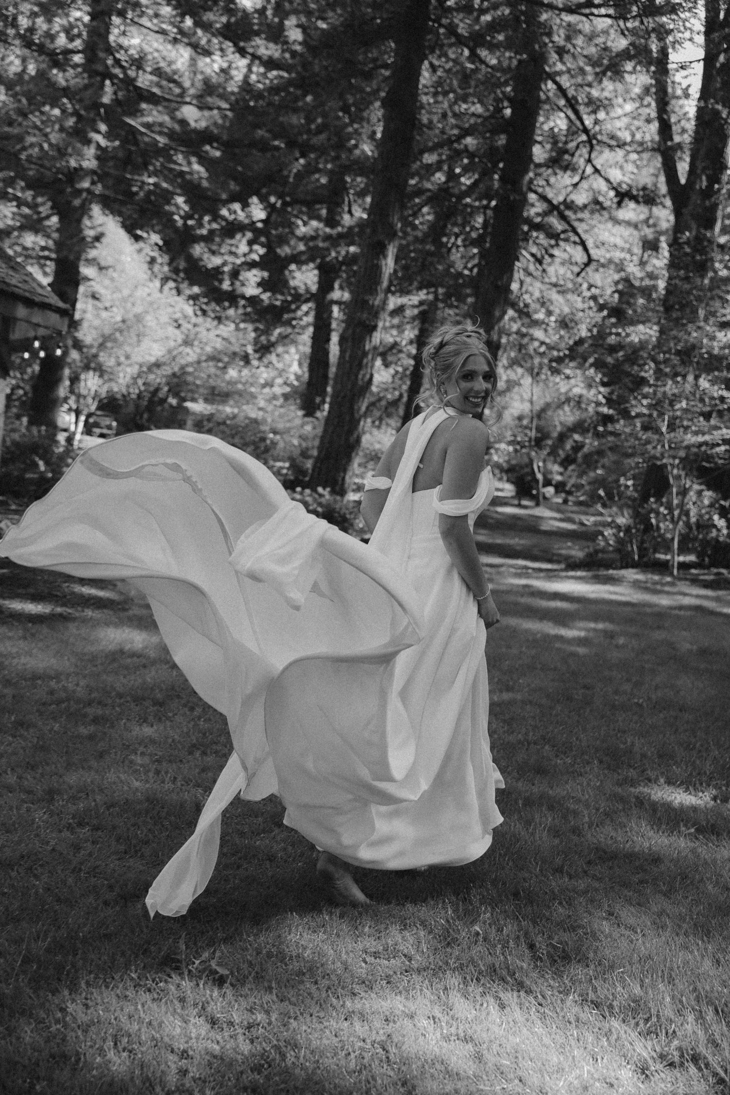 A flowing white wedding dress billows dramatically in the wind during an outdoor forest photoshoot.