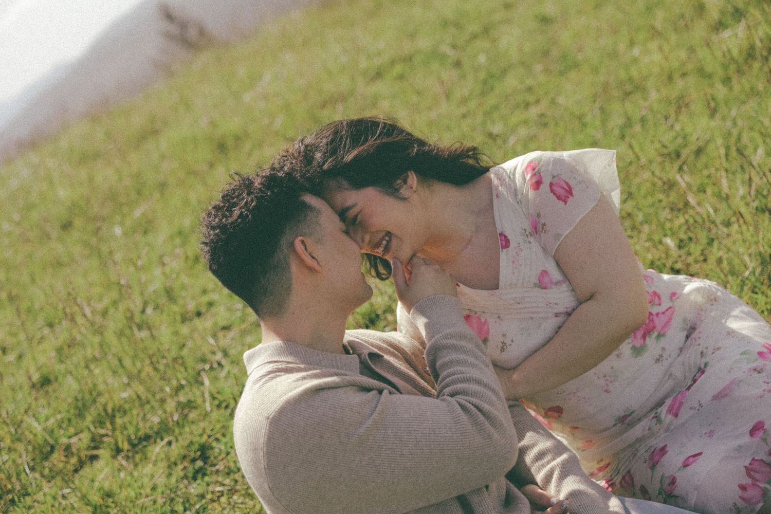 A couple shares an intimate moment while resting on grassy hillside during golden hour.