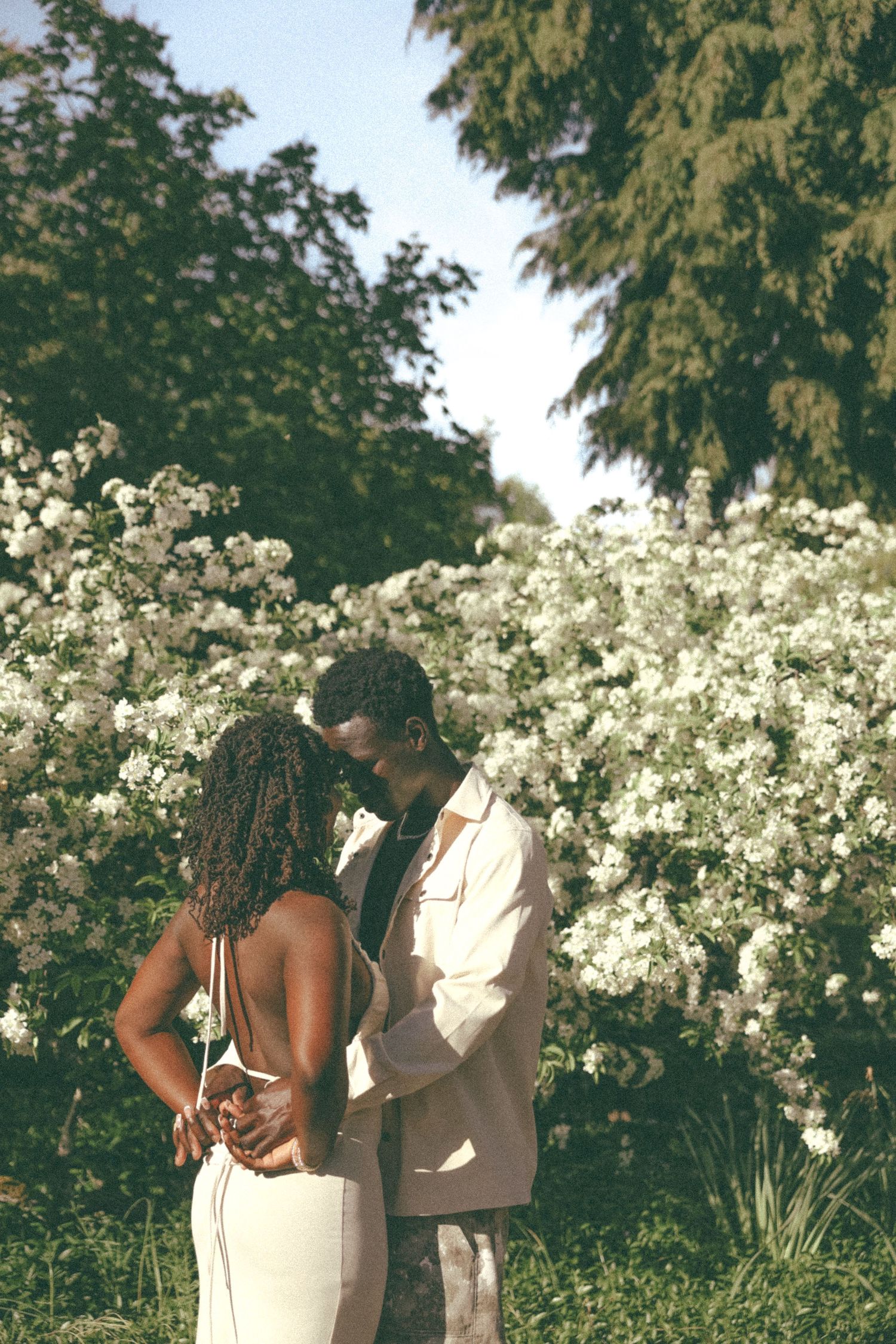 A romantic couple shares an intimate moment in a dreamy garden setting with white flowers.