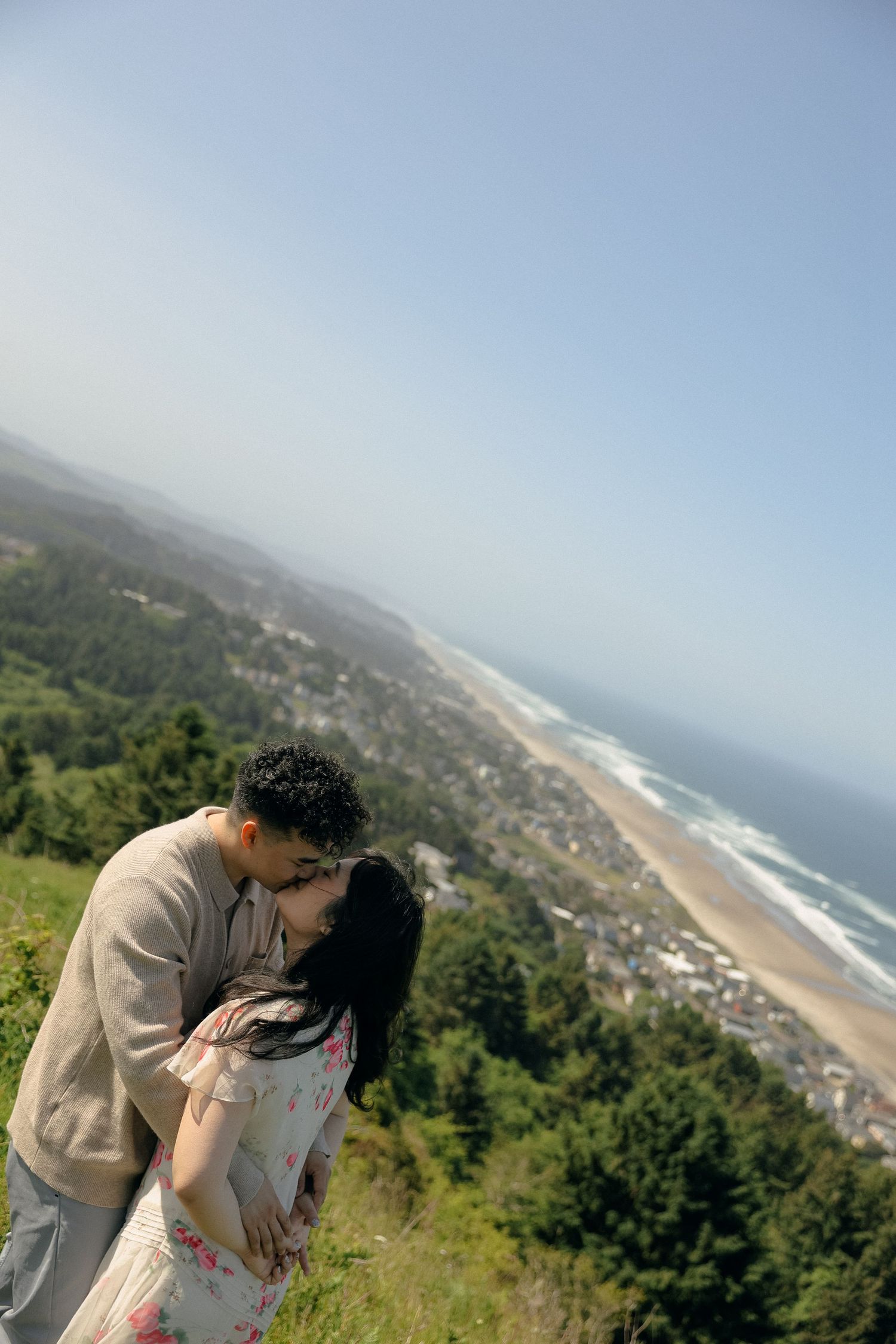 Couple embraces while overlooking a scenic coastal vista with mountains and ocean in the background.