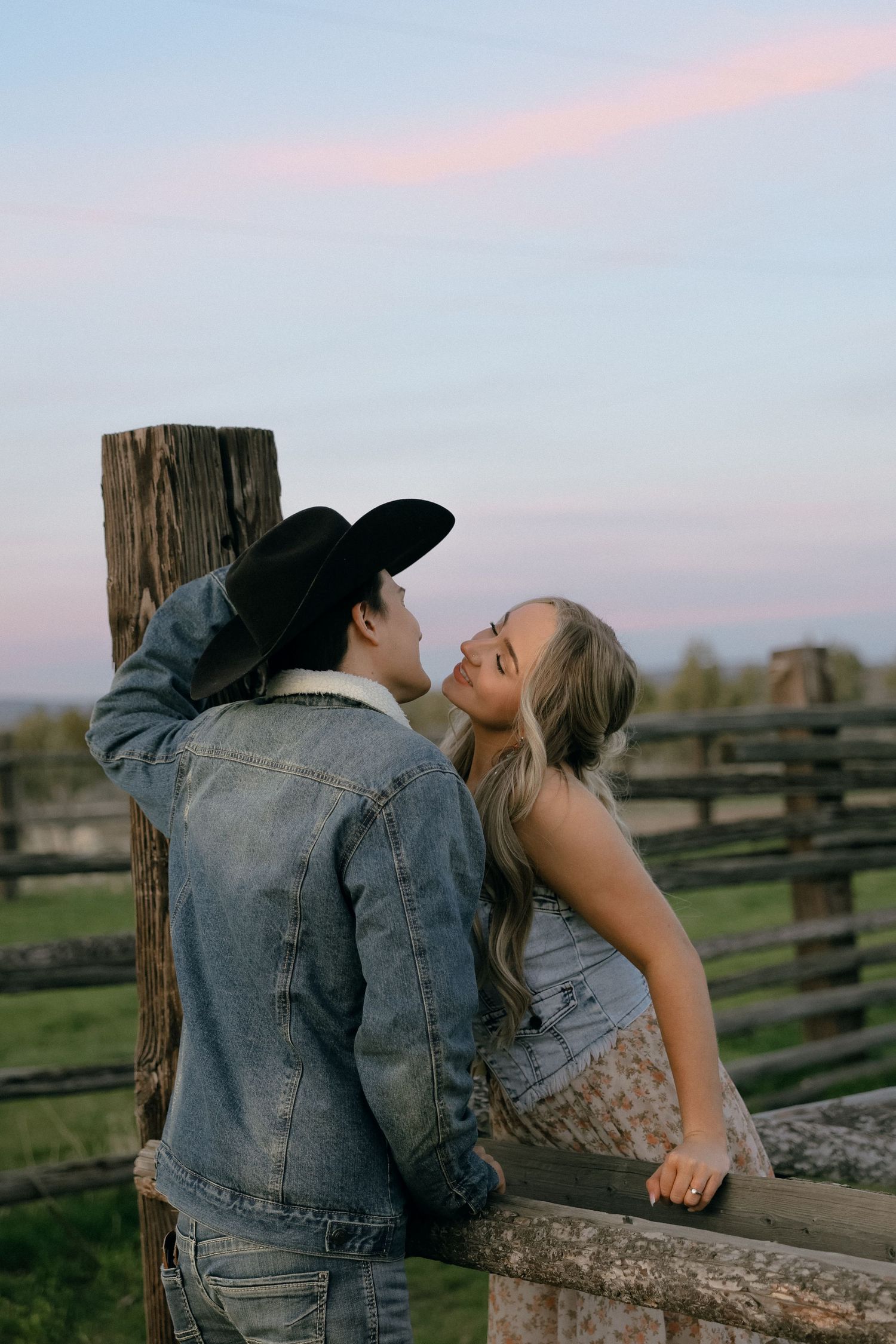 Romantic couple sharing intimate moment against rustic fence during sunset in countryside setting.