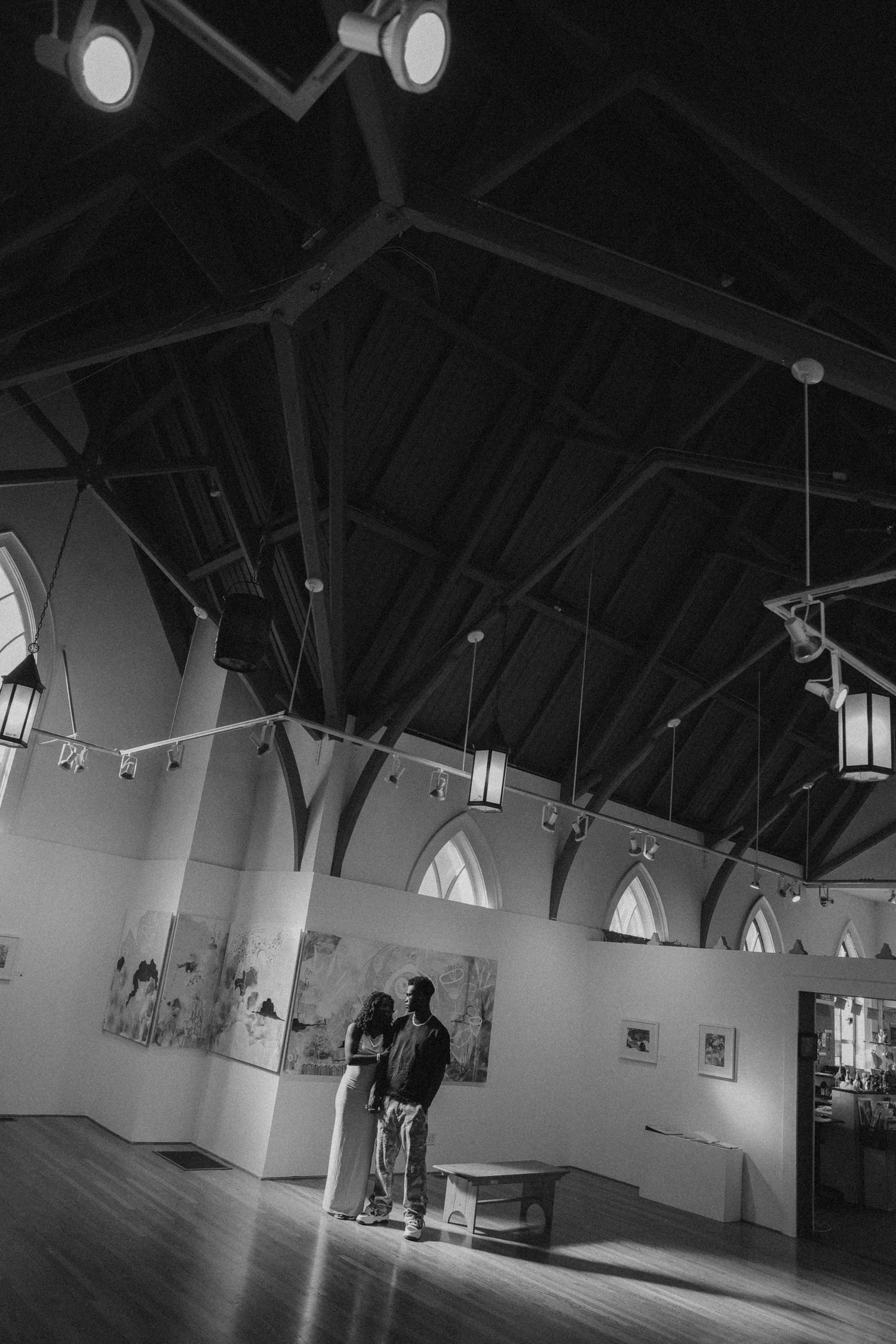 A couple stands in an empty art gallery with vaulted ceilings and track lighting.