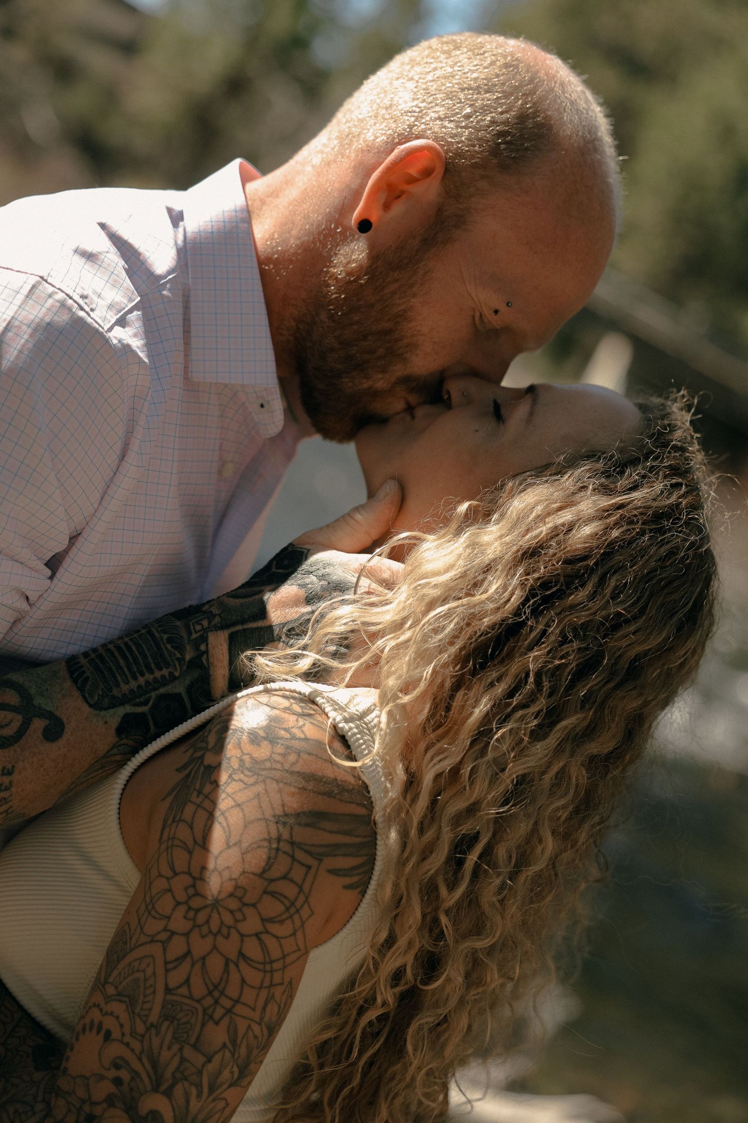 Intimate moments between couple with visible tattoos in natural sunlight.