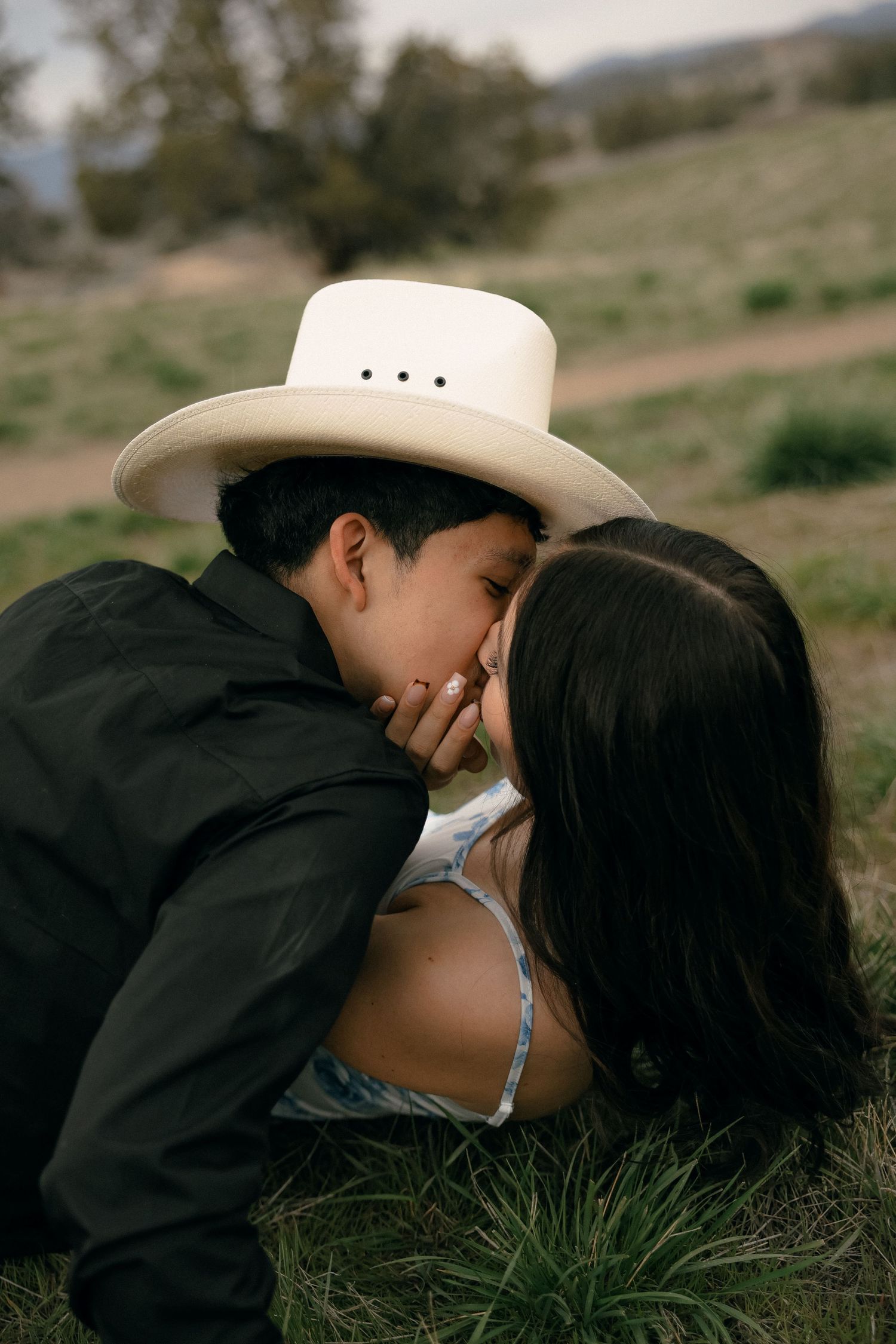 A couple shares an intimate moment while lying in grass on a hillside.