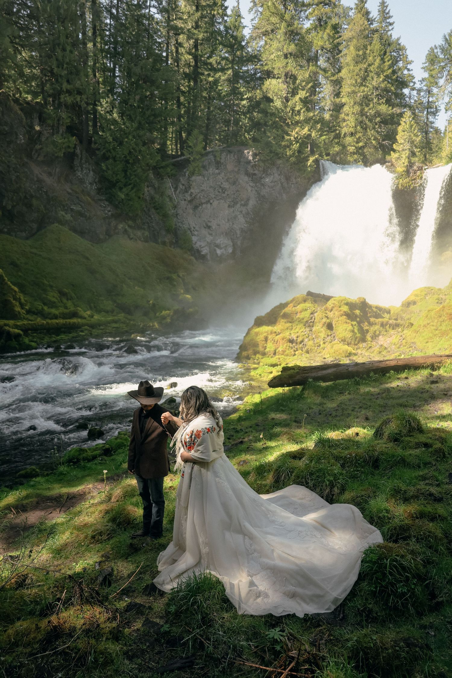 Wedding photos captured near a majestic waterfall with flowing white dress movements in golden sunlight.