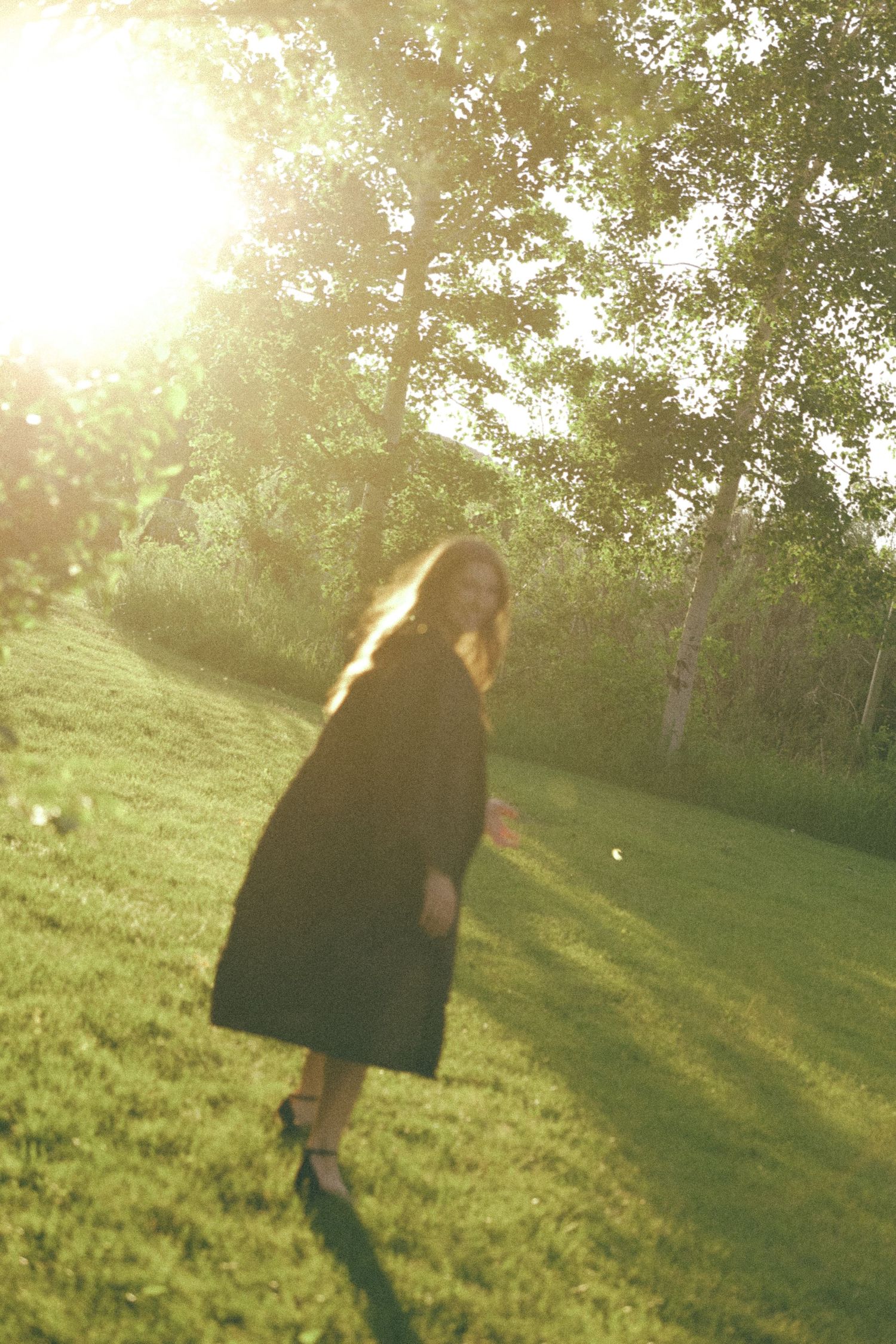 Silhouette of a spinning figure in black dress dancing on grassy hill at golden sunset.