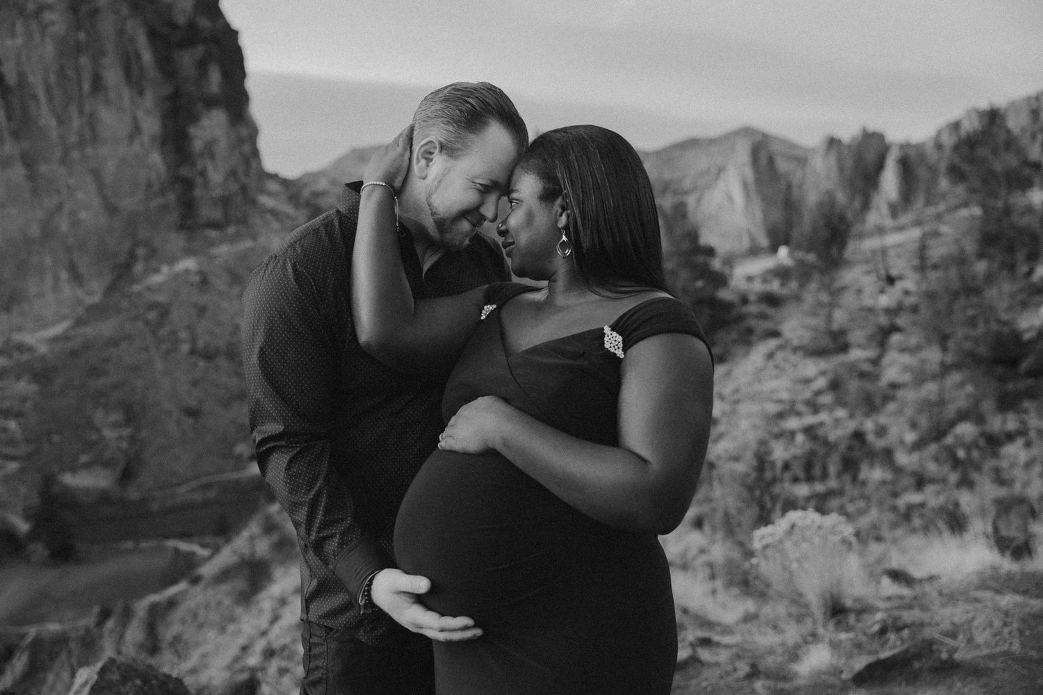 Intimate black and white maternity photo with mountain landscape backdrop.