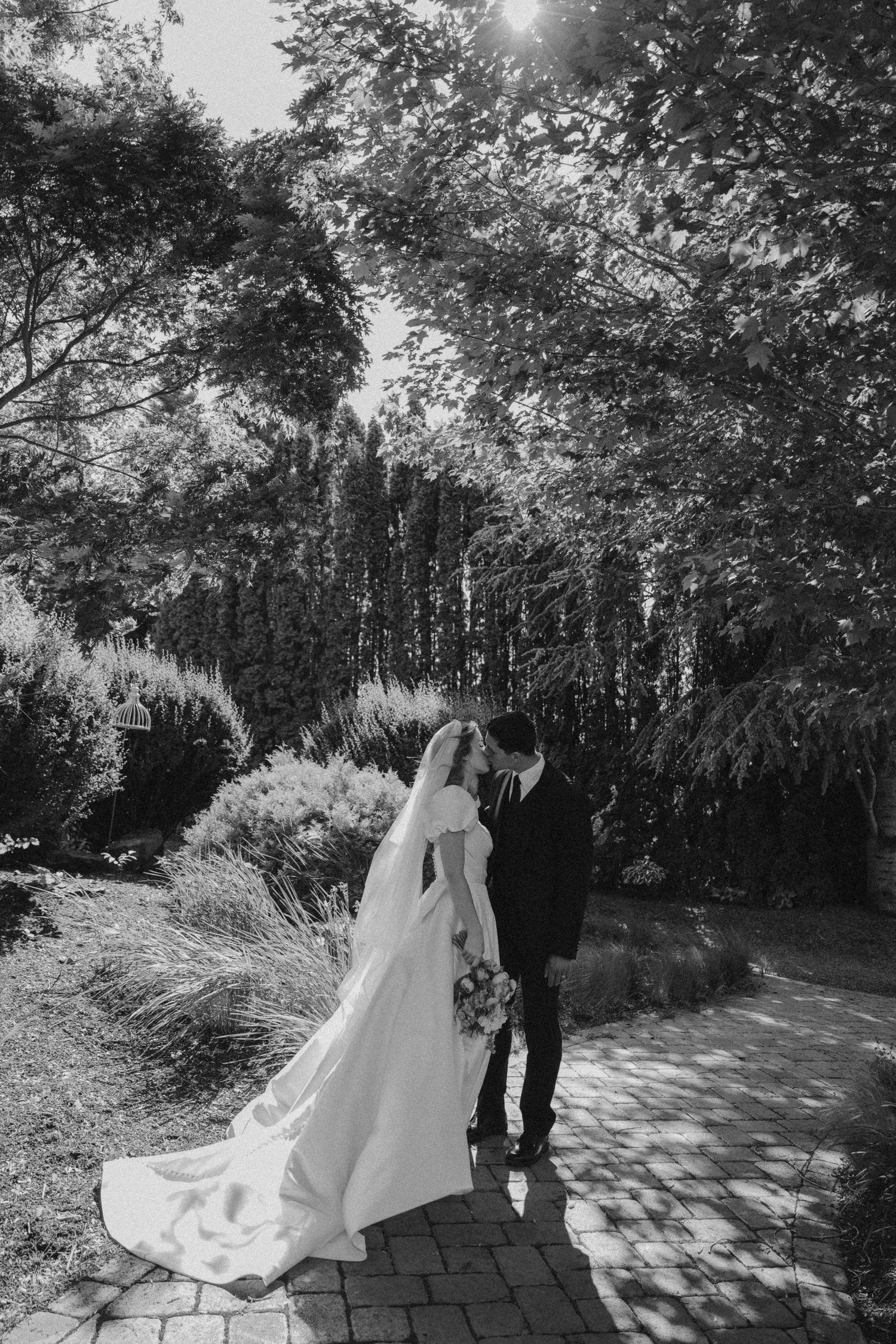 A dreamy wedding photoshoot in a sunlit garden path with trailing white flowers.