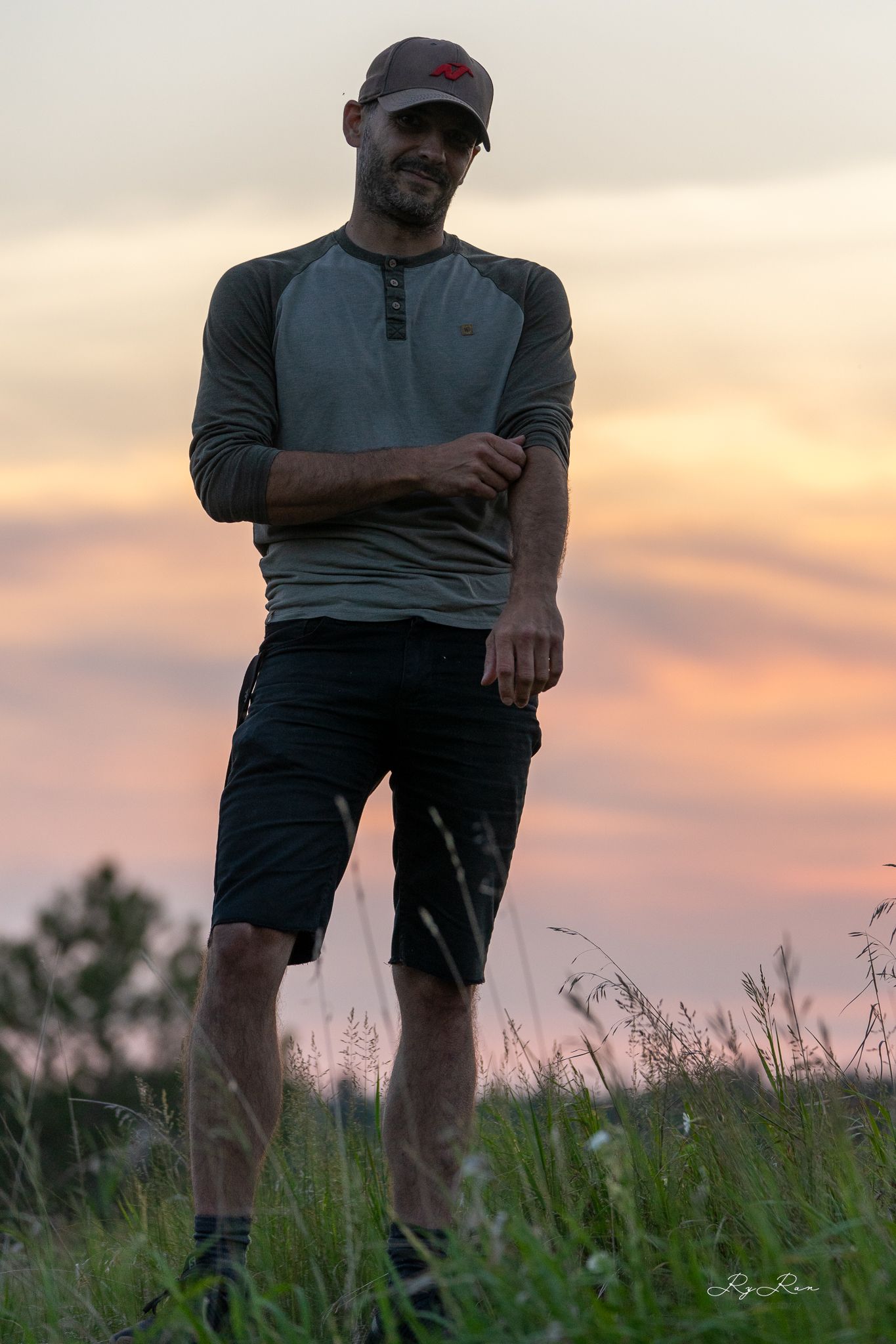 Person in casual athletic wear standing in a field during golden hour sunset.