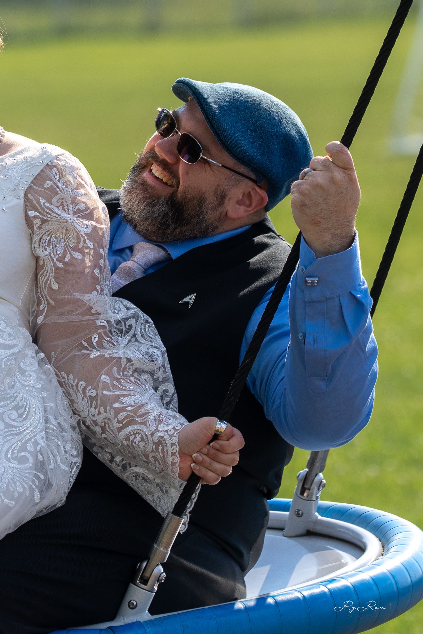 Happy couple enjoying a swing ride in wedding attire and blue jacket.