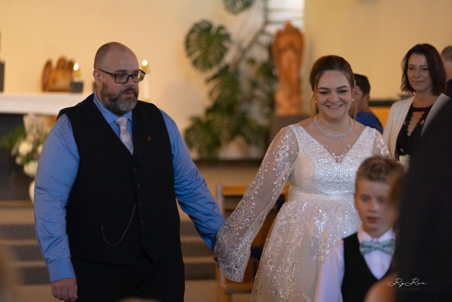 A newlywed couple walking together in a church with guests in the background.