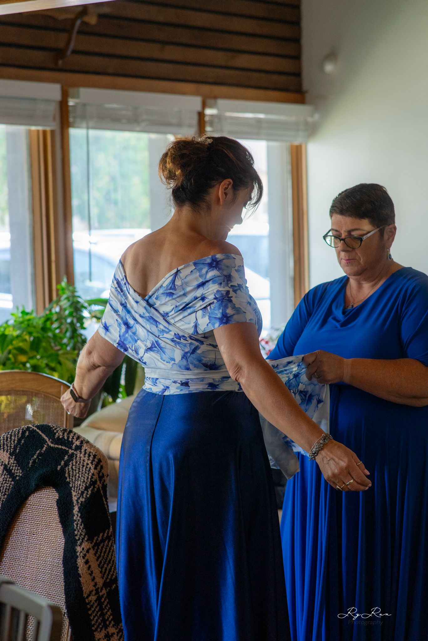 Two people in blue dresses making final preparations in a sunlit room.