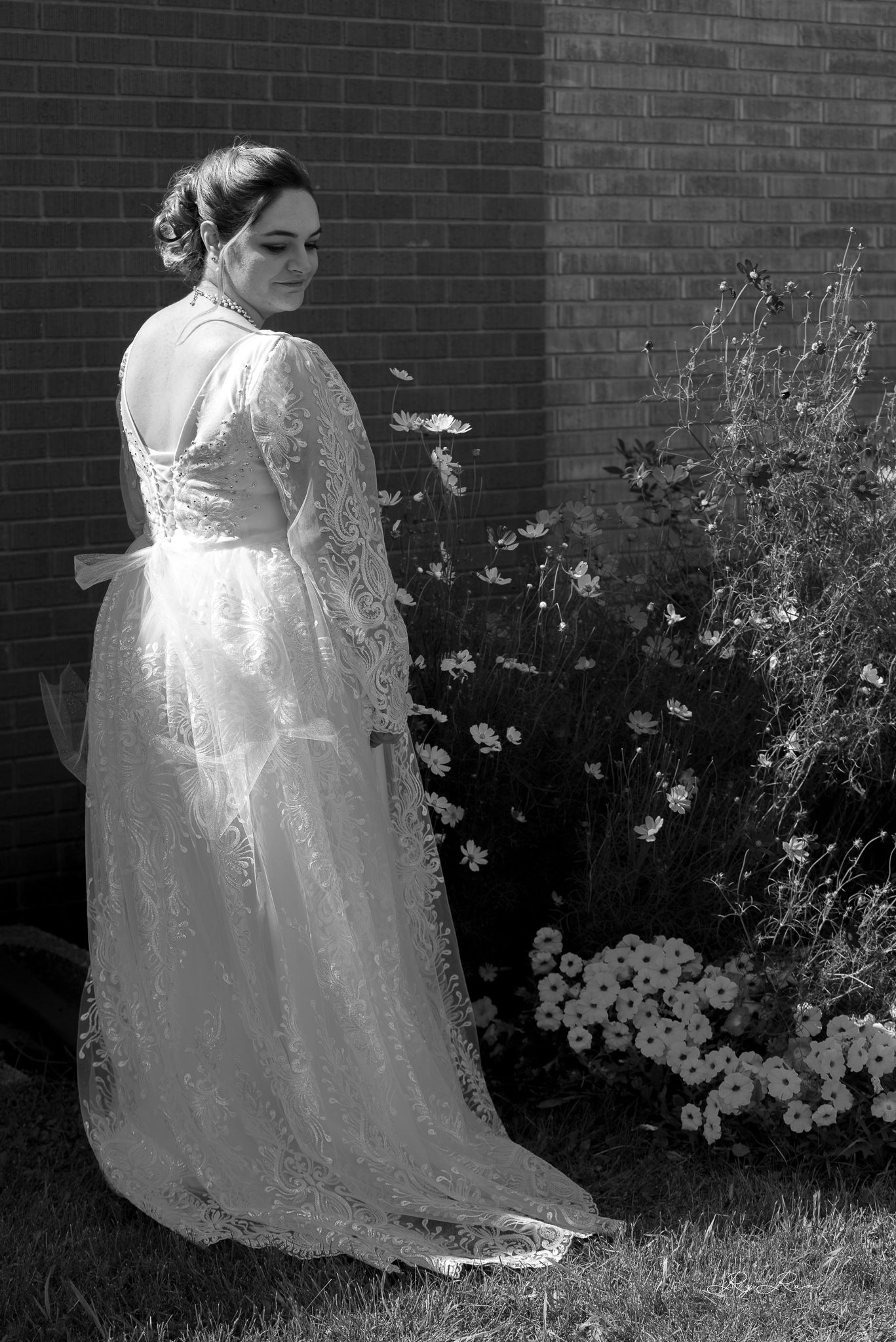 Black and white photo of a wedding dress with long lace sleeves and train against a garden backdrop.