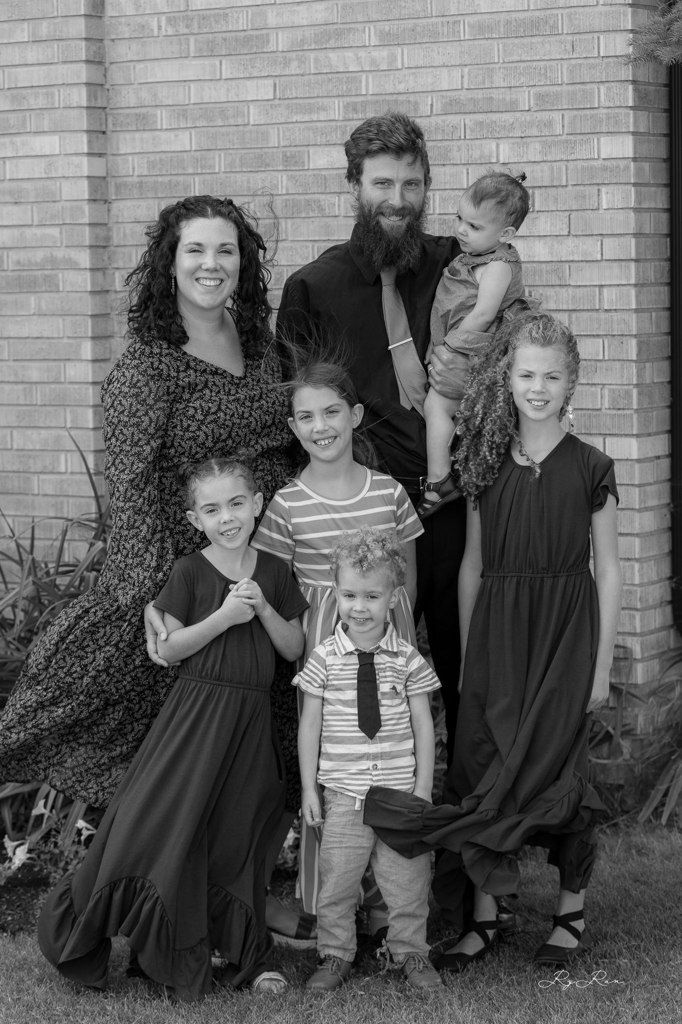 Black and white family portrait with coordinated outfits against brick wall background.