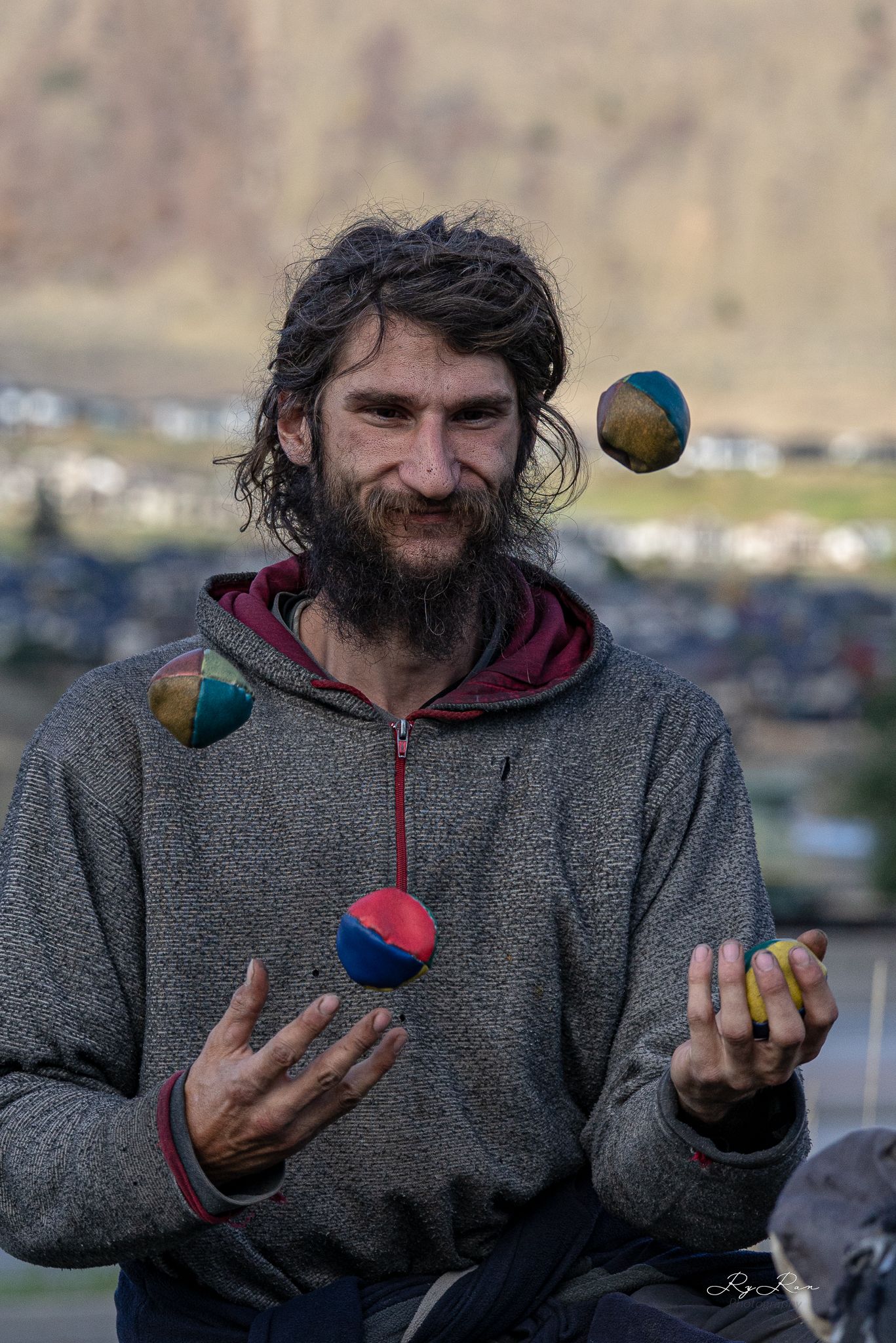 A juggler performs with colorful balls against a mountain backdrop.
