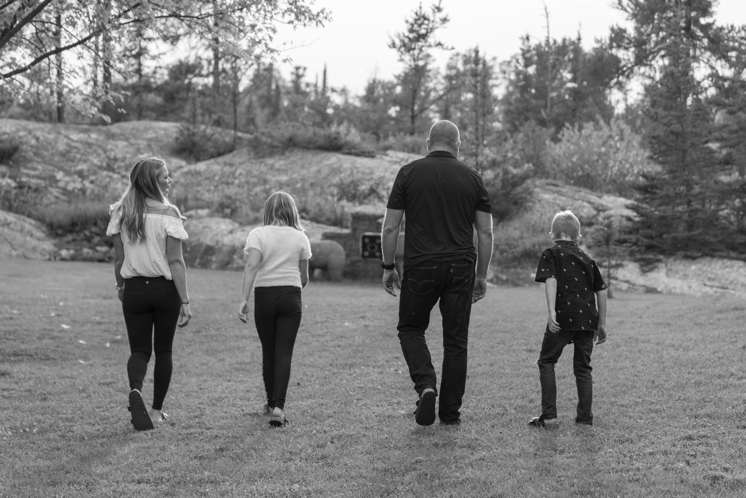 Family walking together across grassy field in black and white photography.