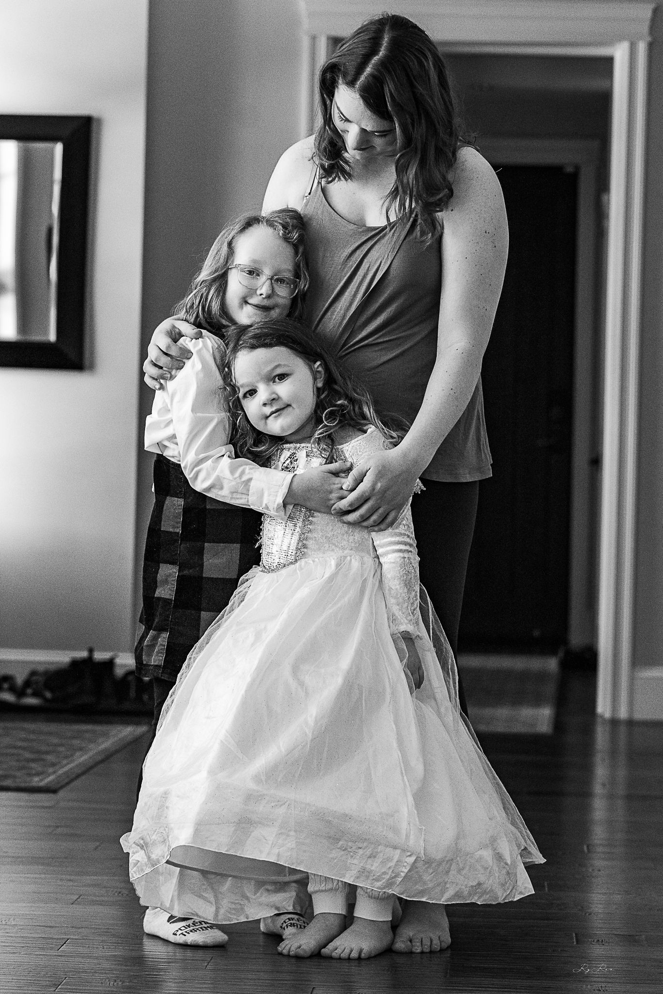A tender family moment captured in black and white as a mother embraces two children in formal attire.