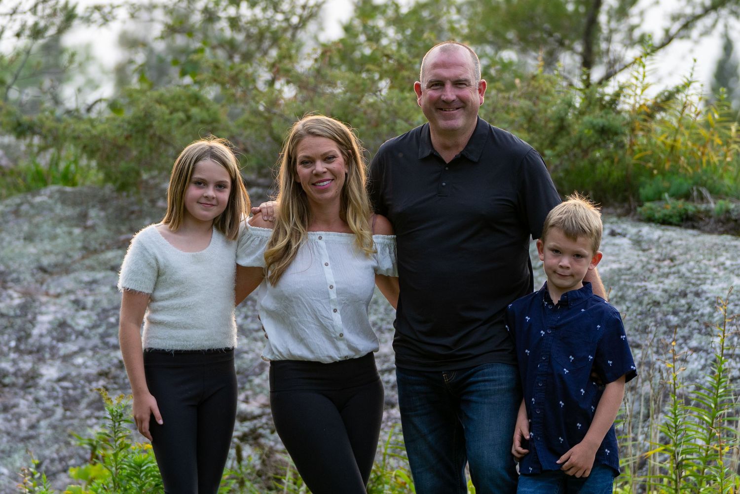 Family portrait of four people standing together outdoors against a natural rocky backdrop.
