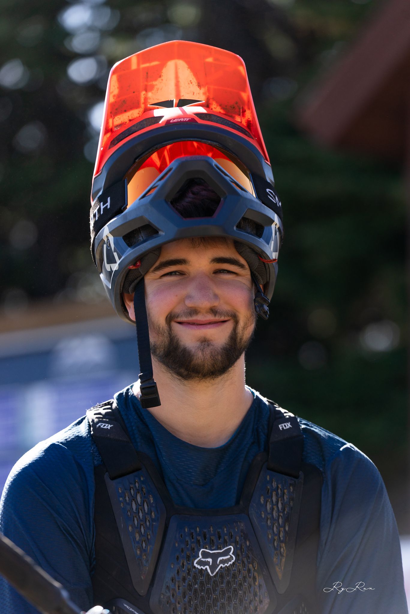 Mountain biker wearing protective gear and orange helmet smiles during outdoor adventure.