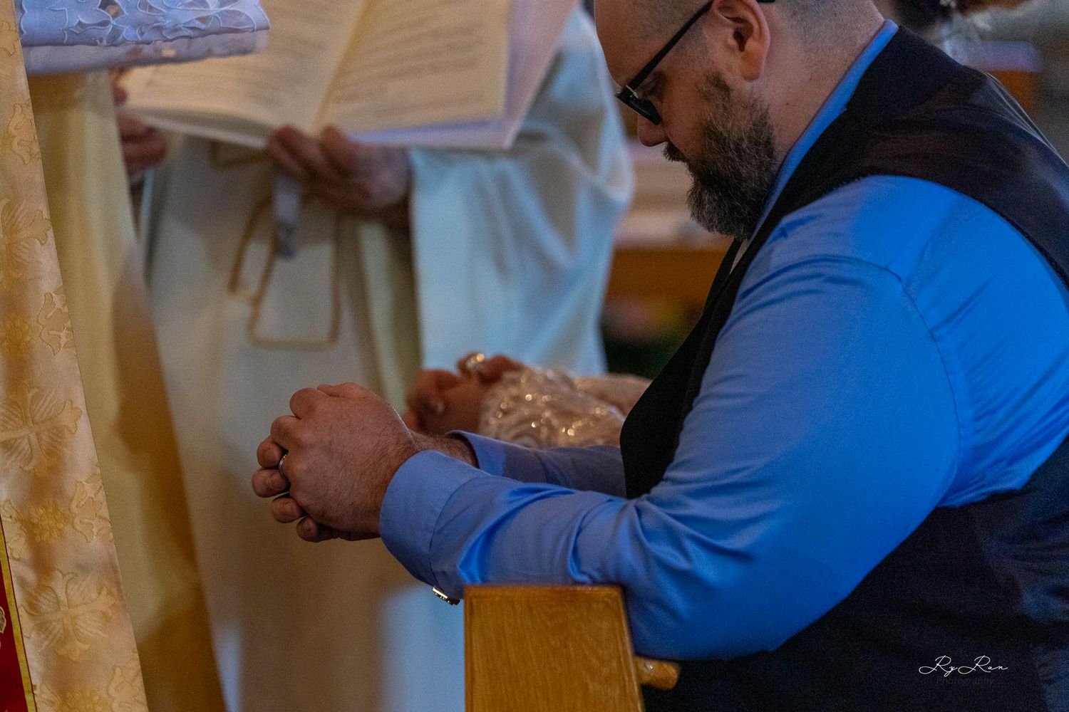A person in a blue shirt holding their hands in prayer during a wedding ceremony.