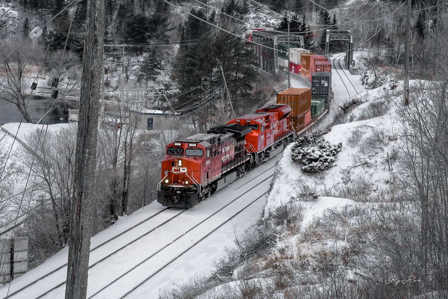Red freight train carrying cargo through snowy winter landscape on mountain tracks.
