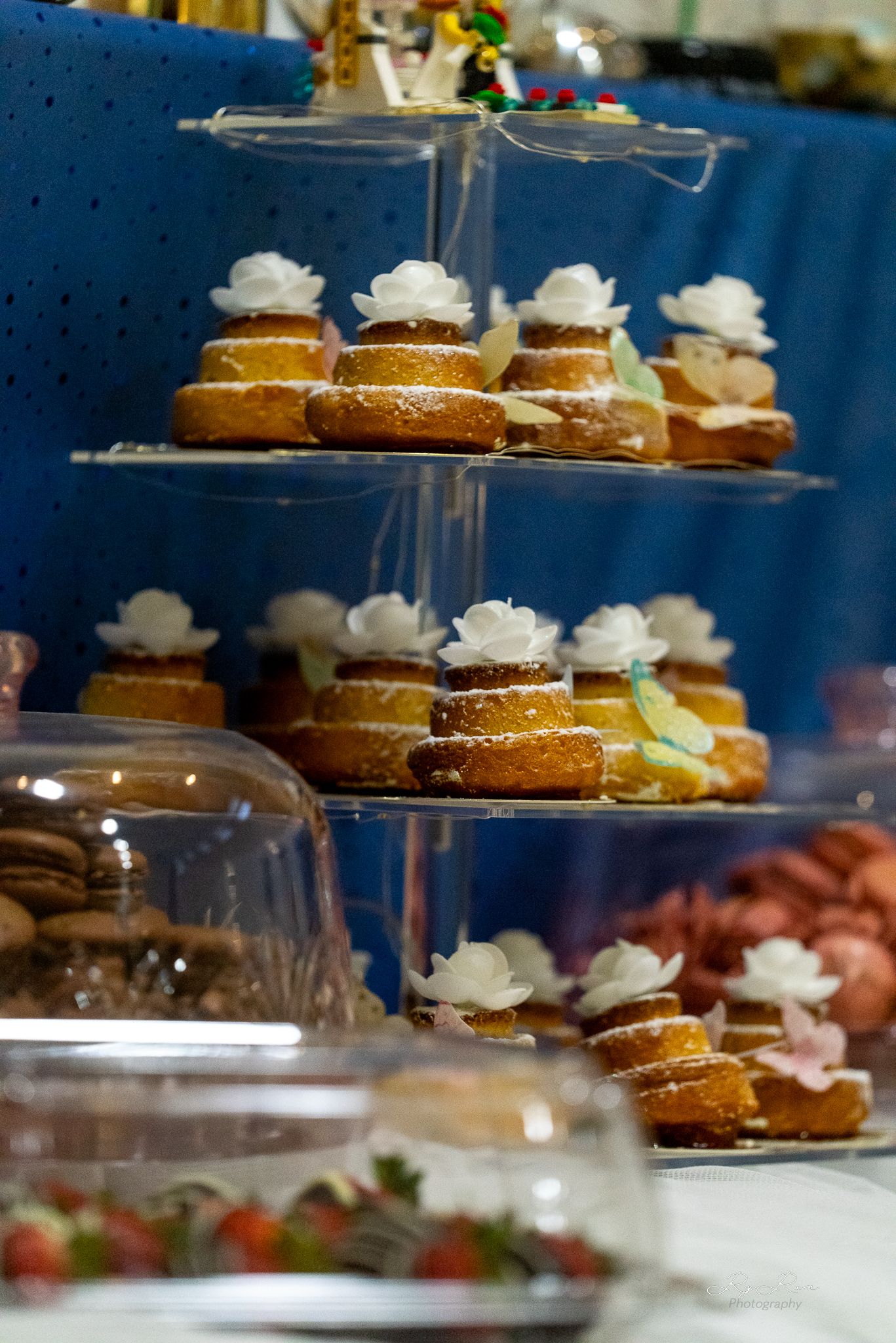 Elegant tiered display of cream-topped mini cakes on a crystal stand with glass domes.