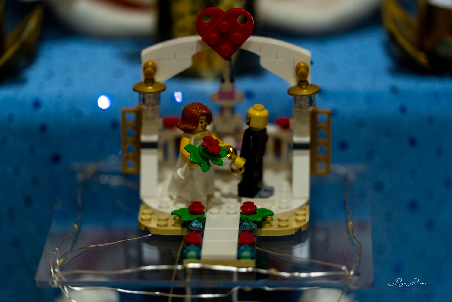 A decorative LEGO wedding cake topper featuring a gazebo with a heart detail on a blue tablecloth.