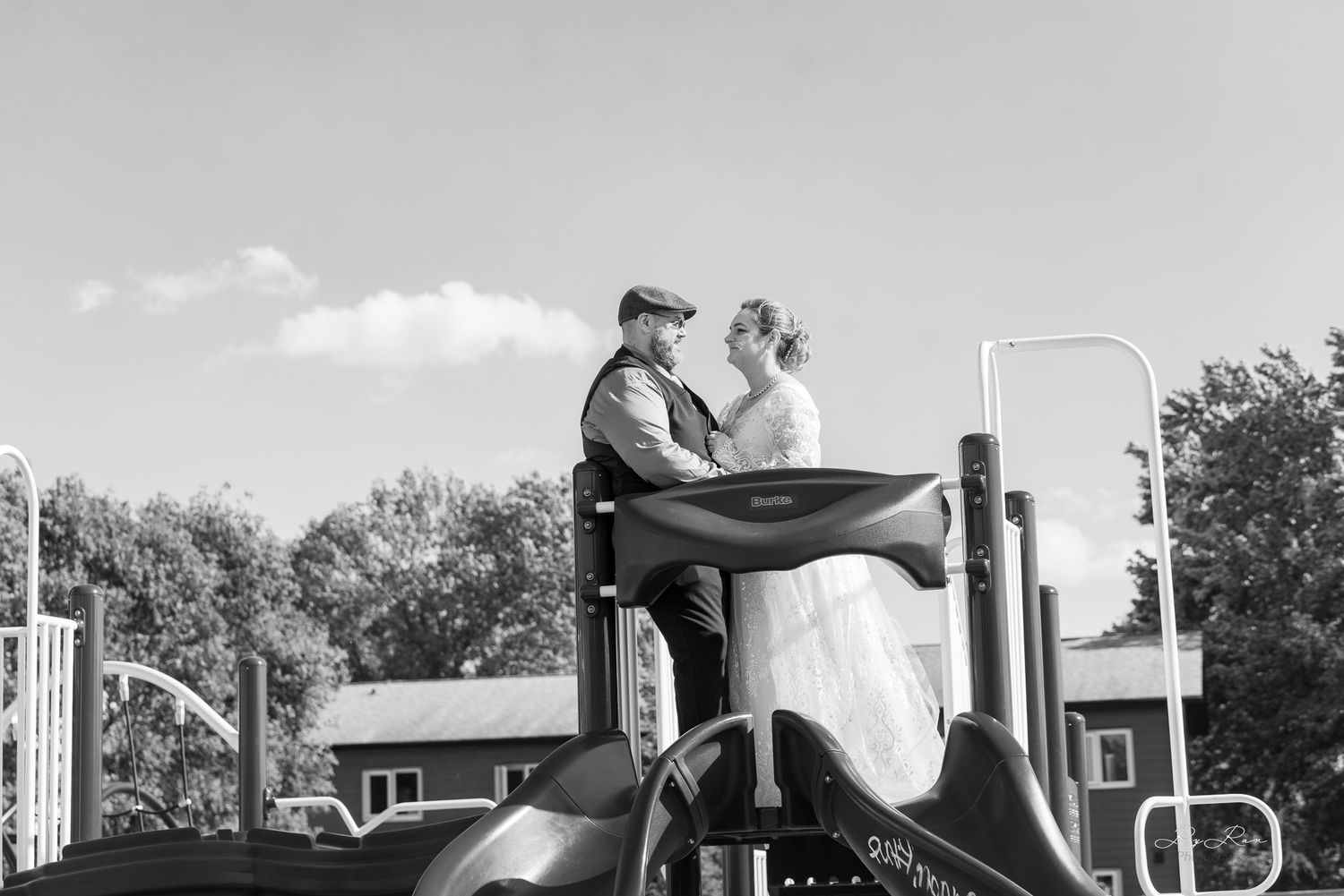 Black and white photo of a couple sitting together on playground equipment during a wedding shoot.