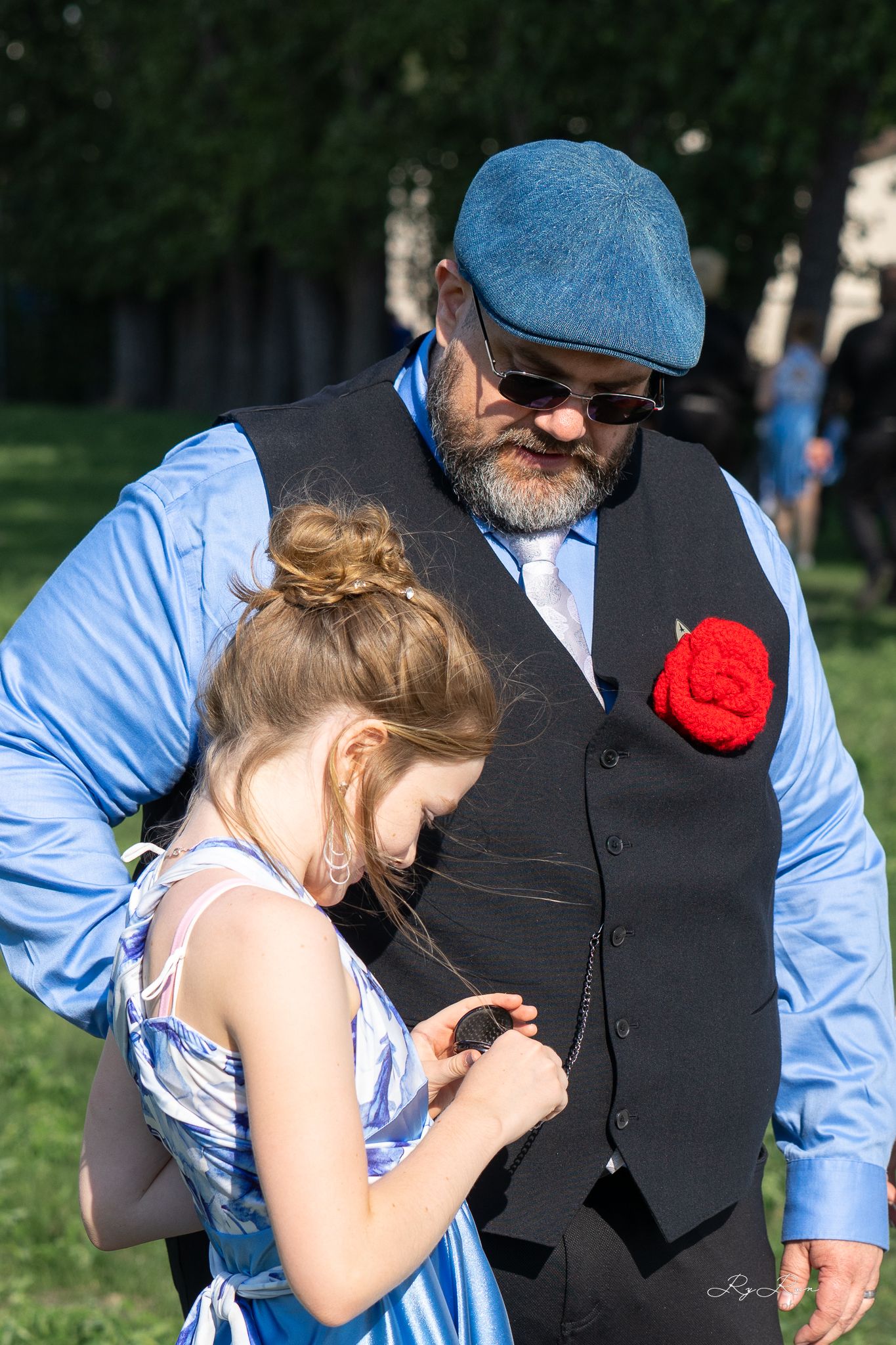 Sweet interaction between formal-dressed duo with bright red boutonniere.