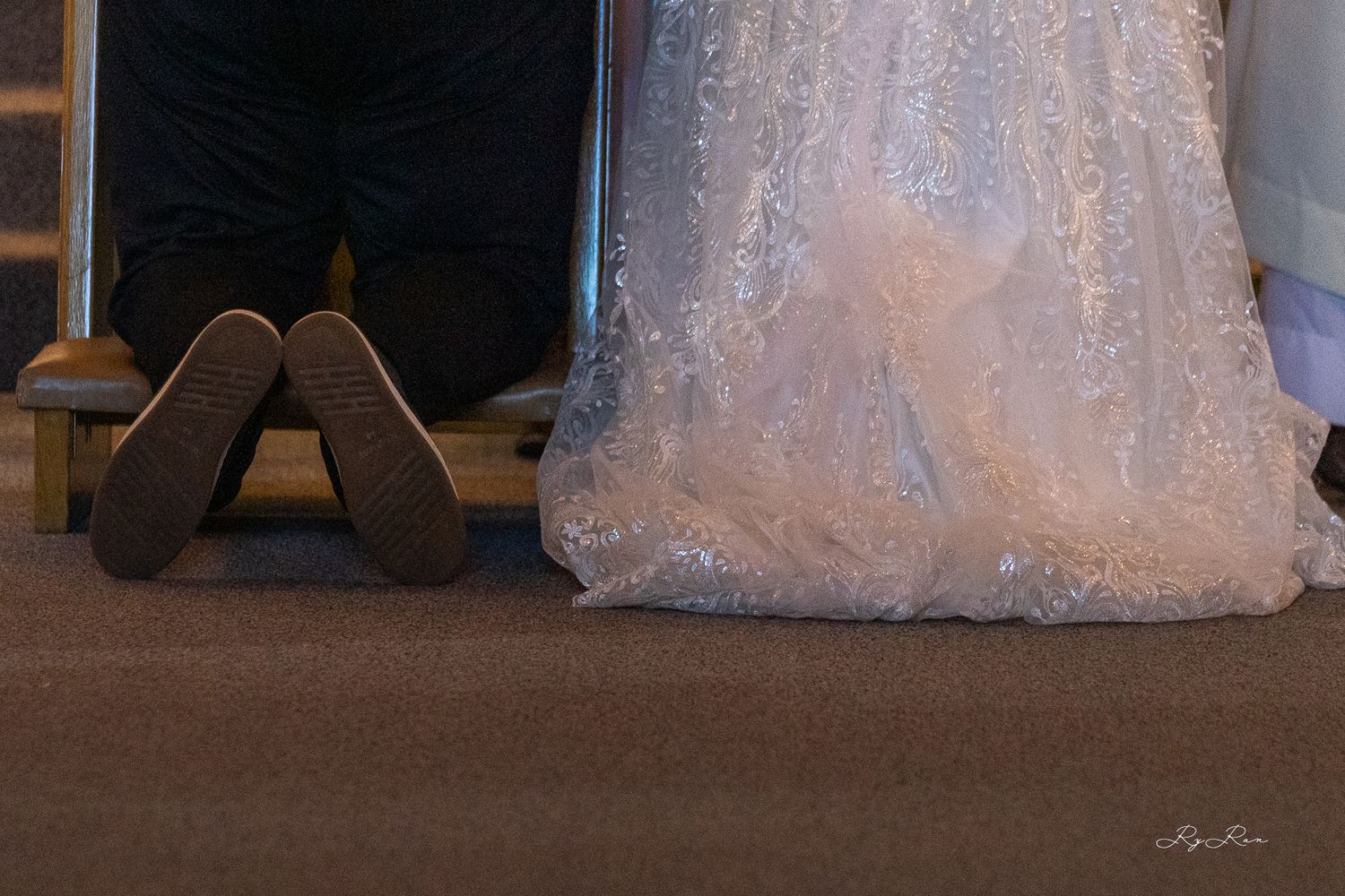 A close-up view of wedding shoes and the hem of a lace wedding dress on carpet.