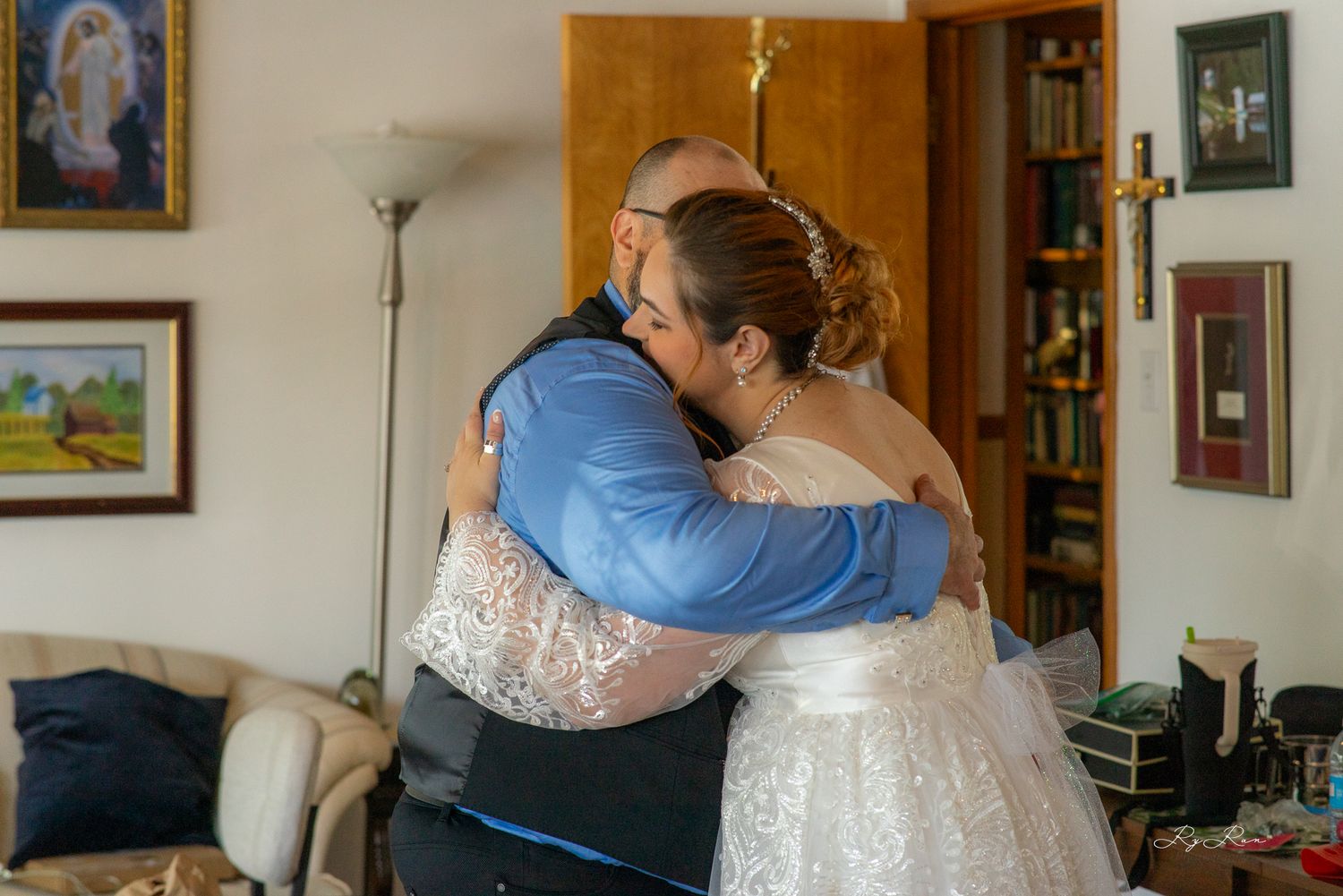 An emotional embracing moment between a bride in white lace and someone in a blue shirt and black vest.