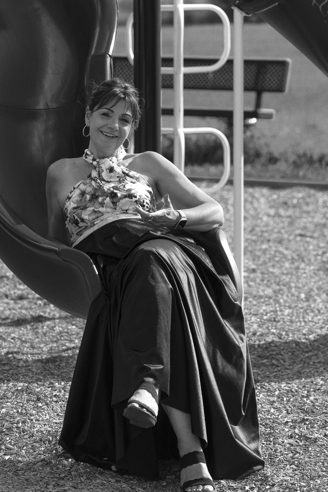 Black and white portrait of woman in formal dress relaxing on playground equipment.
