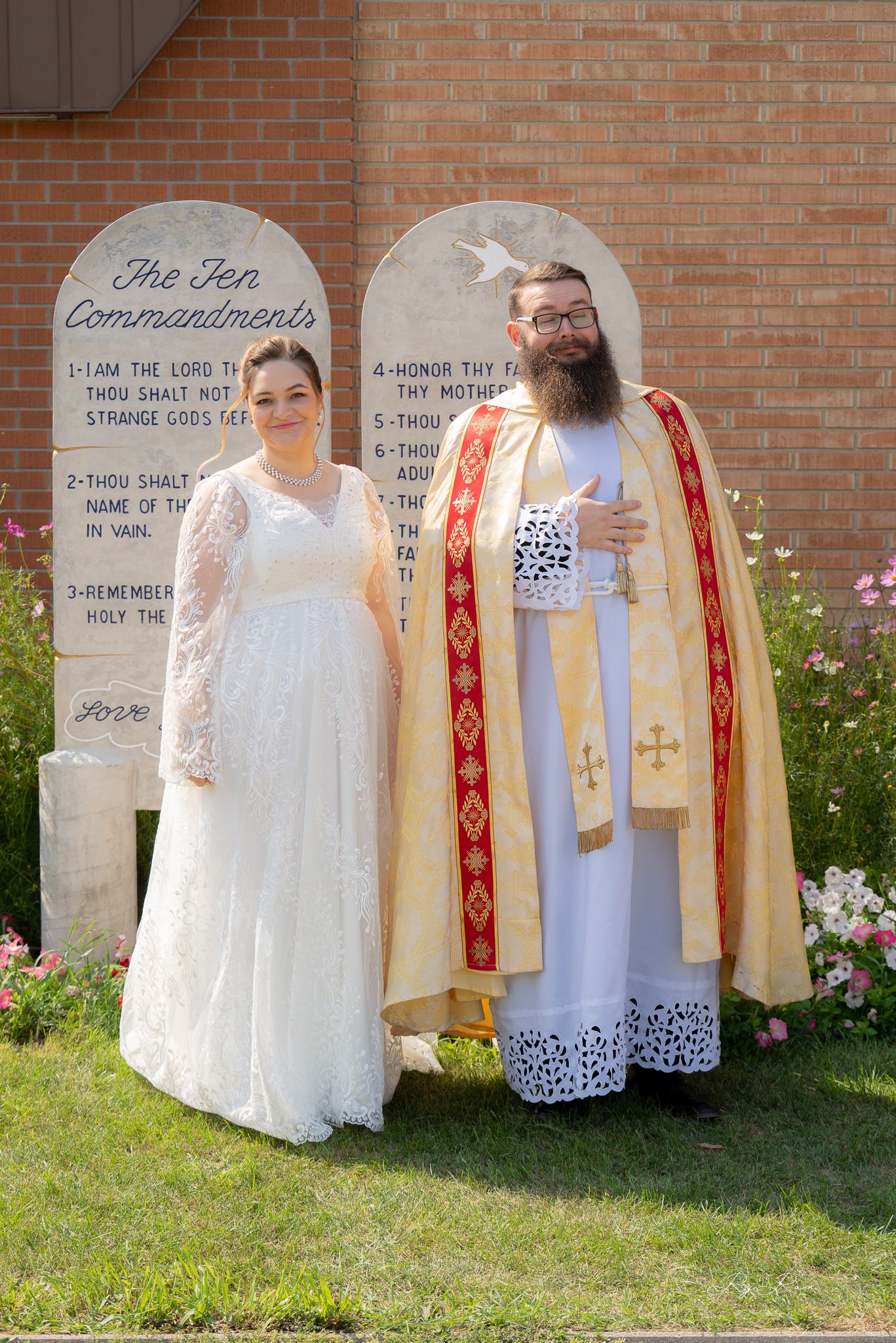 A wedding portrait in front of stone tablets showing a bride and clergy member in ceremonial robes.