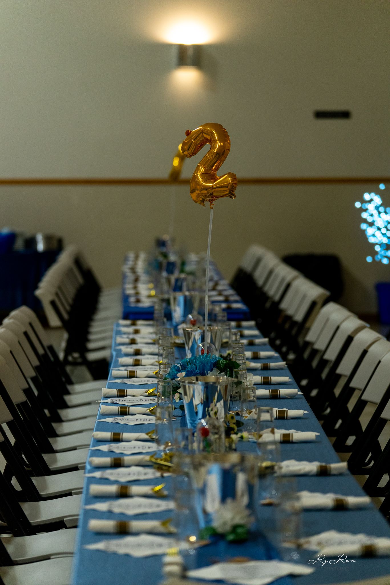Formal dining table with blue runner and golden number 2 balloon centerpiece.