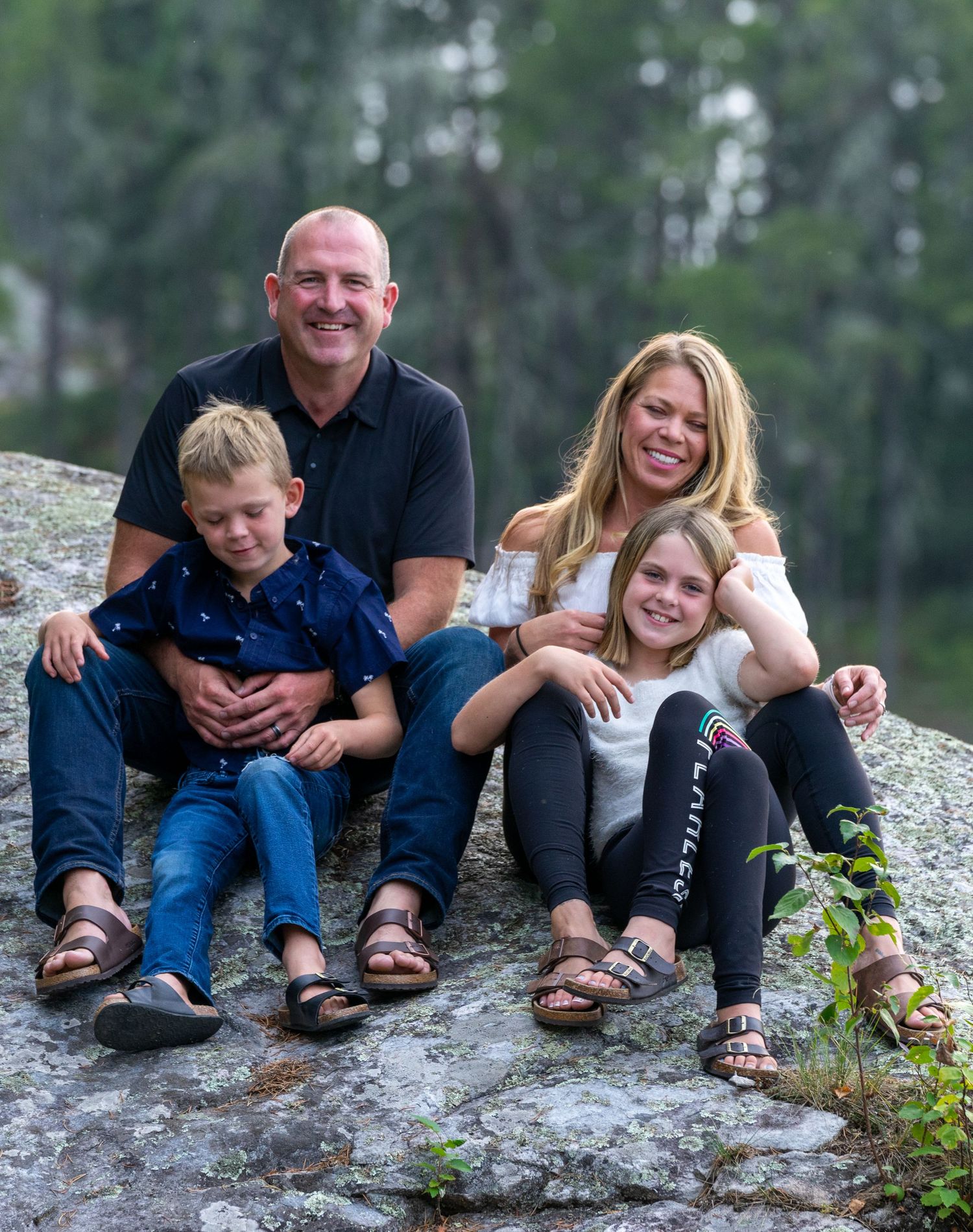 Candid family photo of four people laughing together while sitting on rocky outcrop.