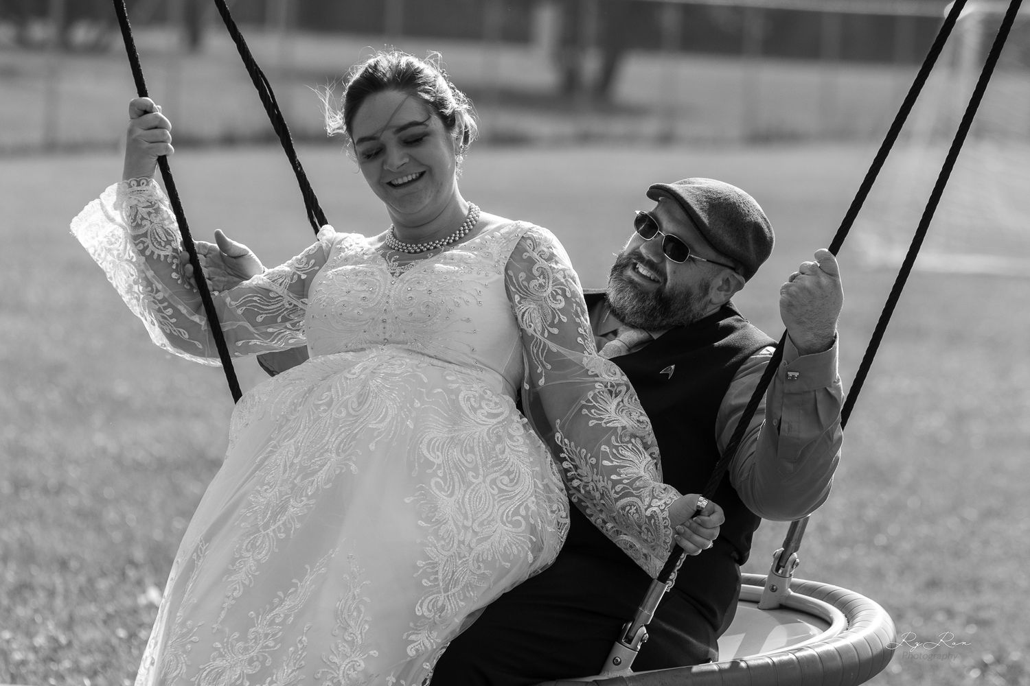 Black and white portrait of newlyweds sharing a joyful moment on a playground swing.