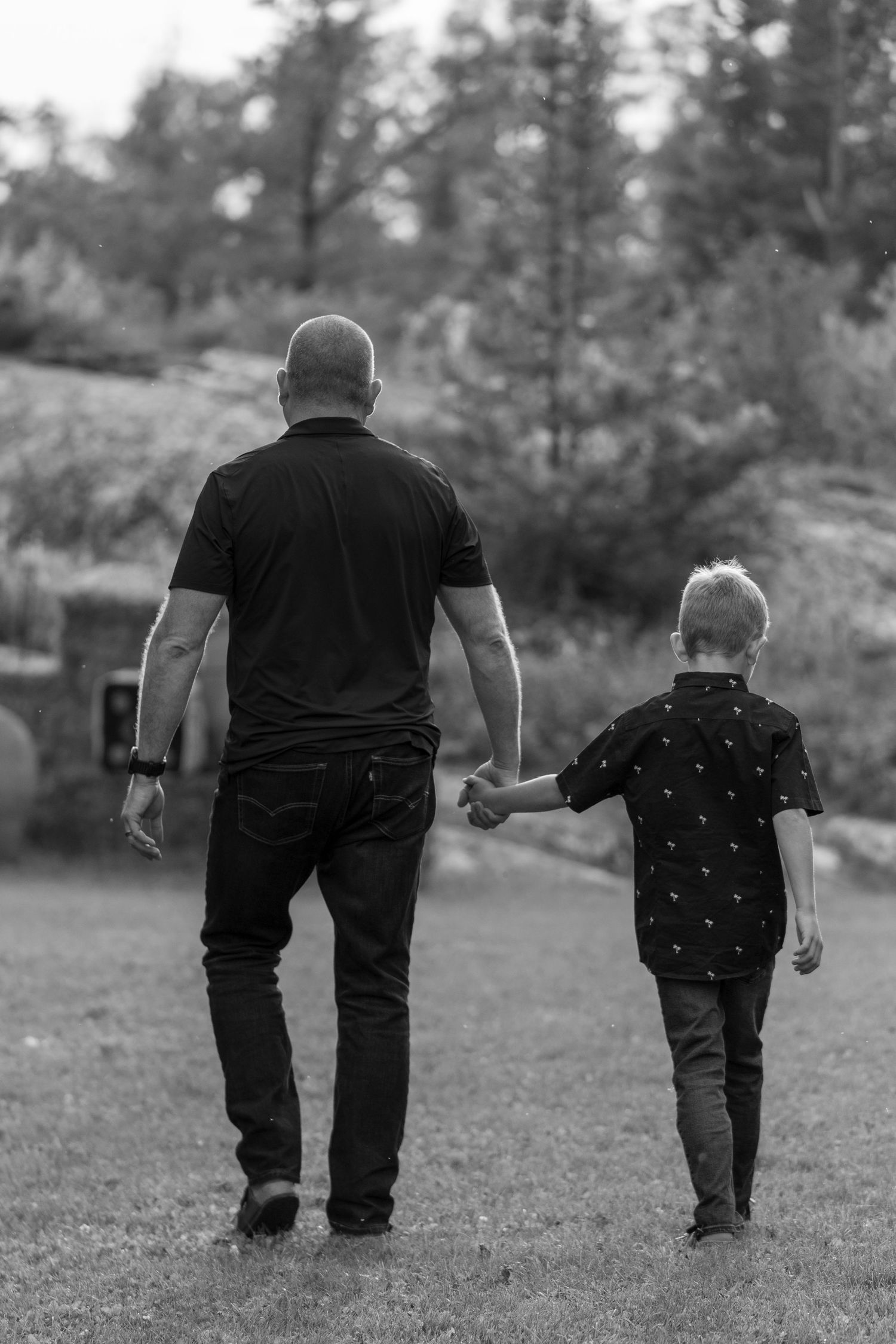 Black and white photo of adult and child walking hand in hand on grass path.