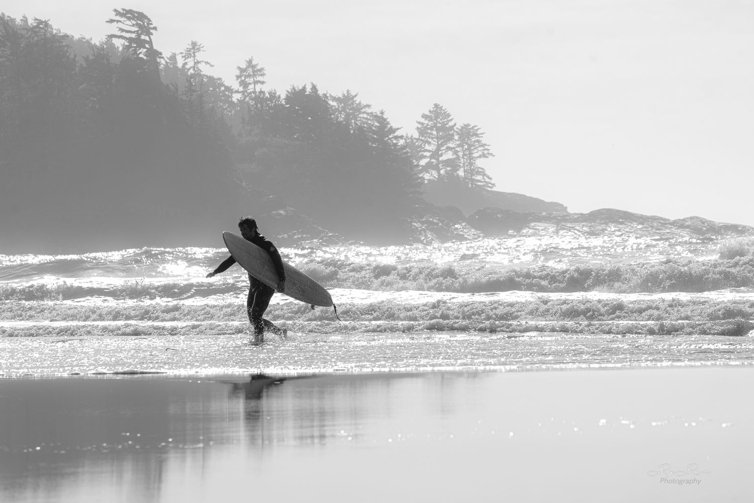 Silhouette of surfer walking along misty beach at dawn.