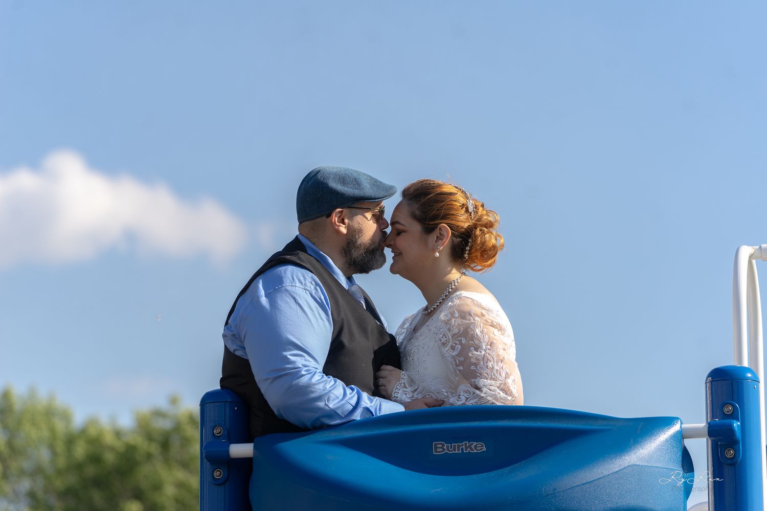 A couple in wedding attire sharing an intimate moment on a blue playground structure.